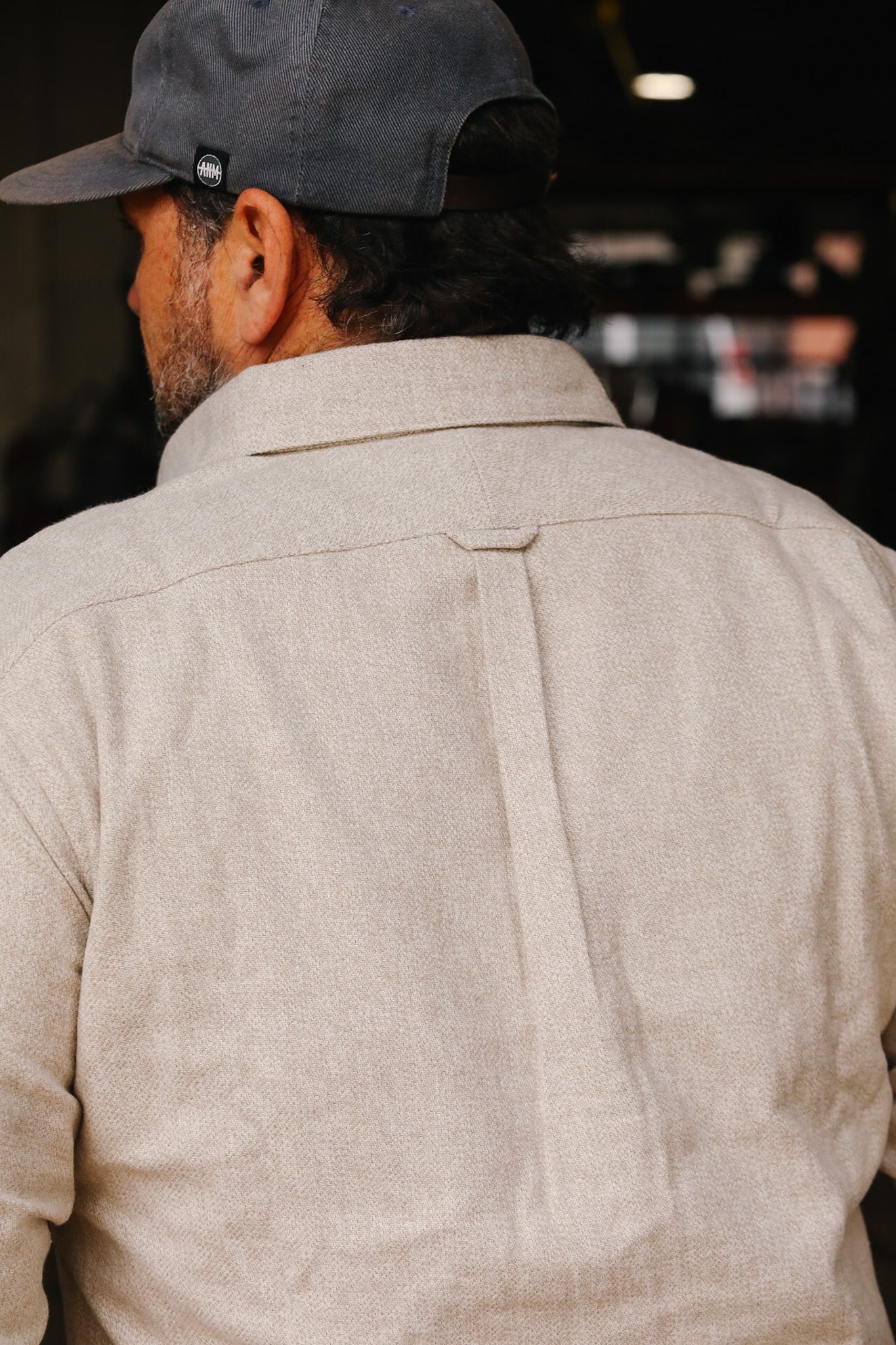 Man wearing cream flannel Oxford shirt with back yoke and center pleat, paired with dark cap