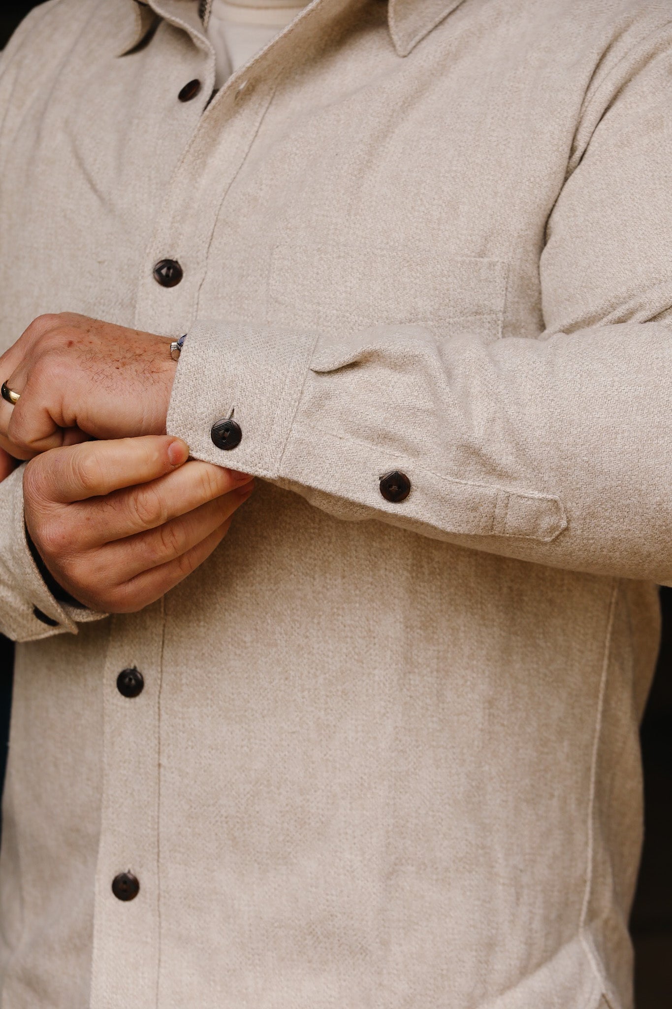 Close-up of man adjusting cuff on cream flannel Oxford shirt with dark buttons at Iron Shop Provisions
