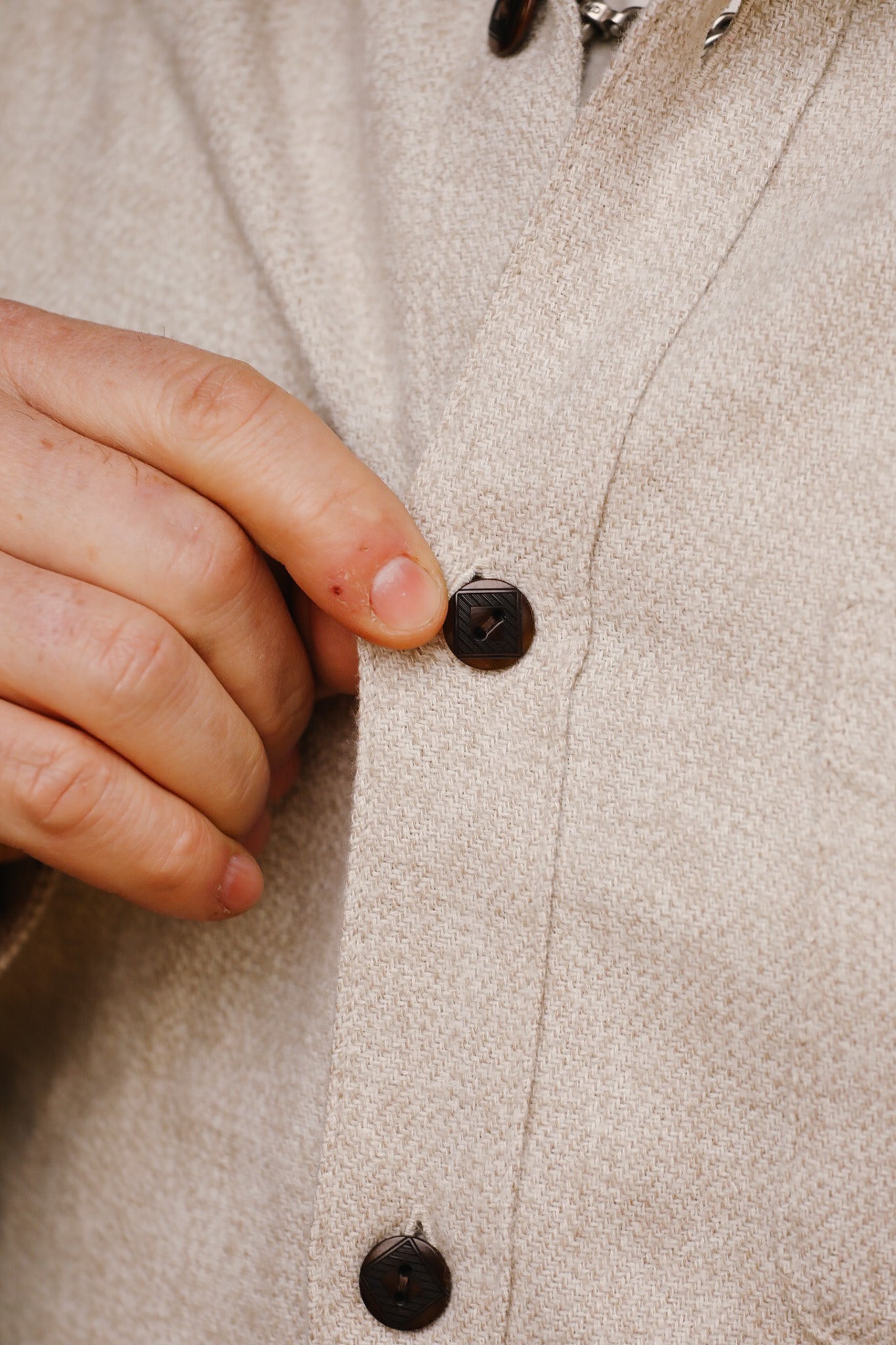 Close-up of hand buttoning cream-colored flannel Oxford shirt with dark buttons
