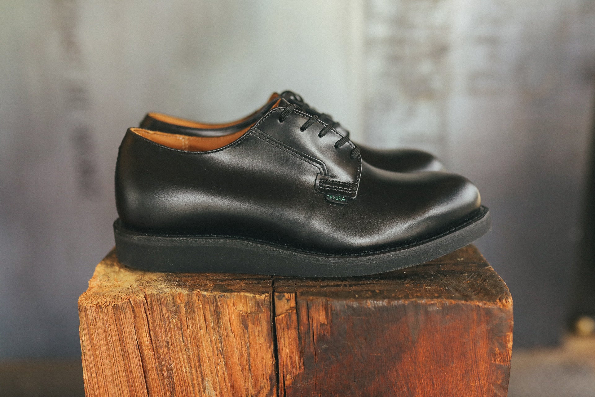 Pair of black leather Postman Oxford dress shoes with laces displayed on a rustic wooden block