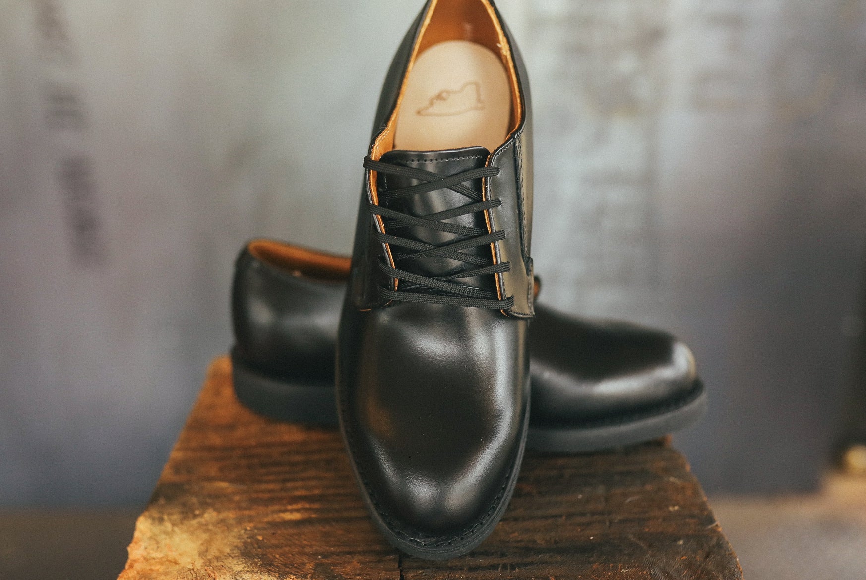 Black leather Postman Oxford shoes with laces on wooden surface in rustic setting