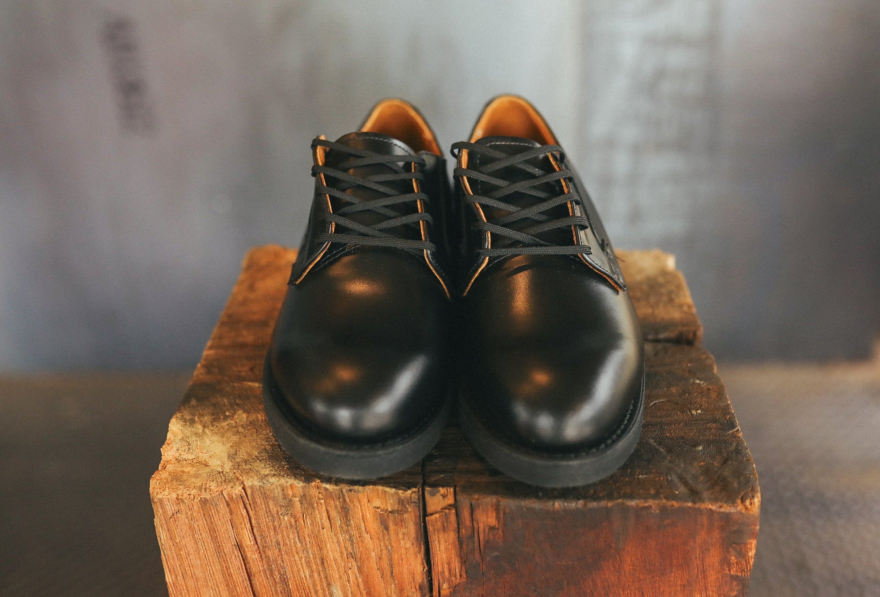 Pair of black leather Postman Oxford shoes displayed on rustic wooden block