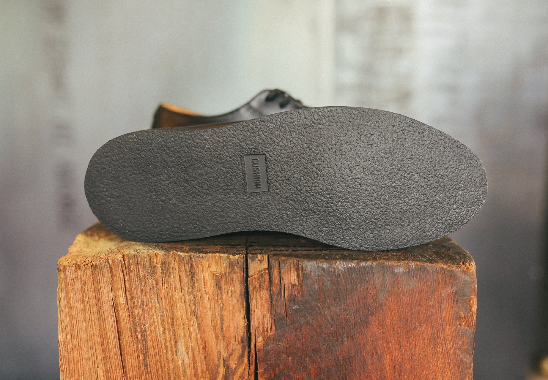 Black Postman Oxford shoe sole with cushioned texture on rustic wooden block