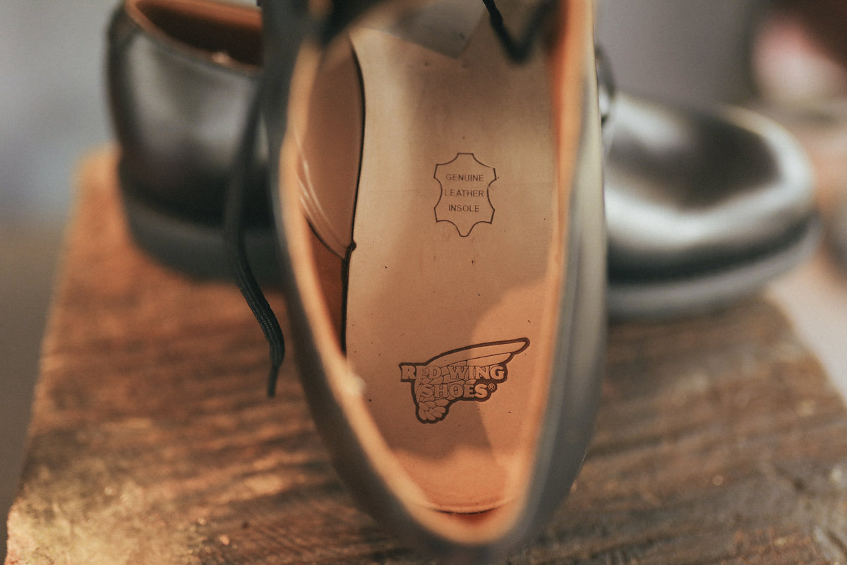 Close-up of Black Postman Oxfords shoe with genuine leather insole and Red Wing Shoes logo on wooden surface