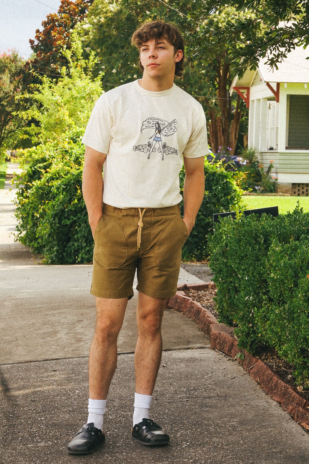 Young man standing on a sidewalk with greenery and a house in the background