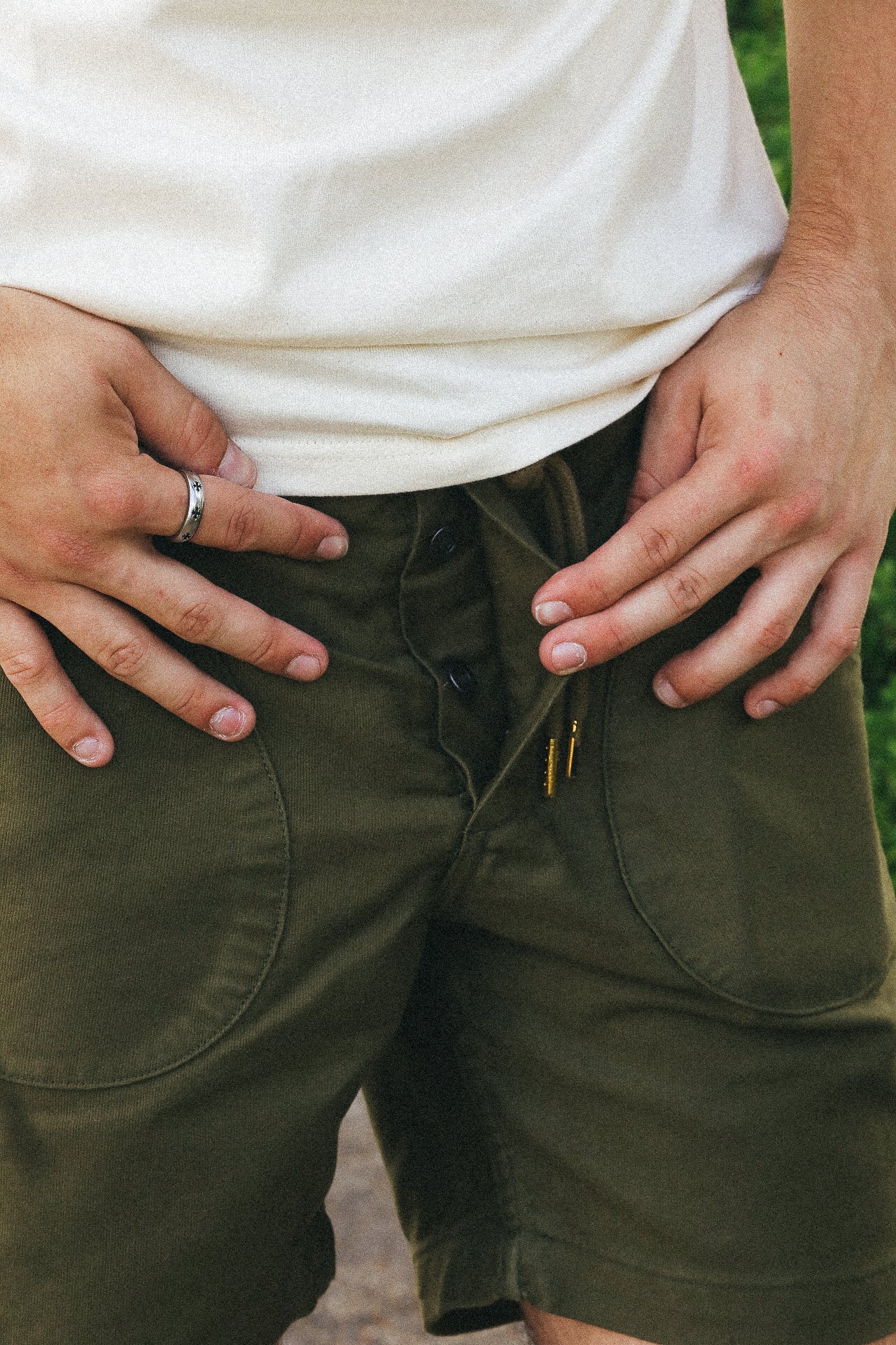 Close-up of man wearing olive green buttoned shorts and a white shirt with hands resting on hips