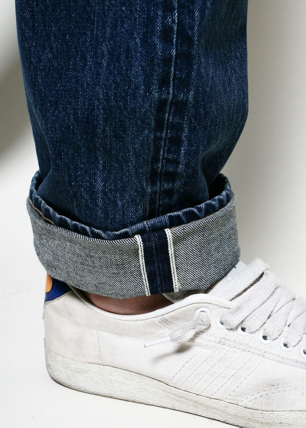 Close-up of rolled-up dark blue denim jeans paired with white canvas sneakers