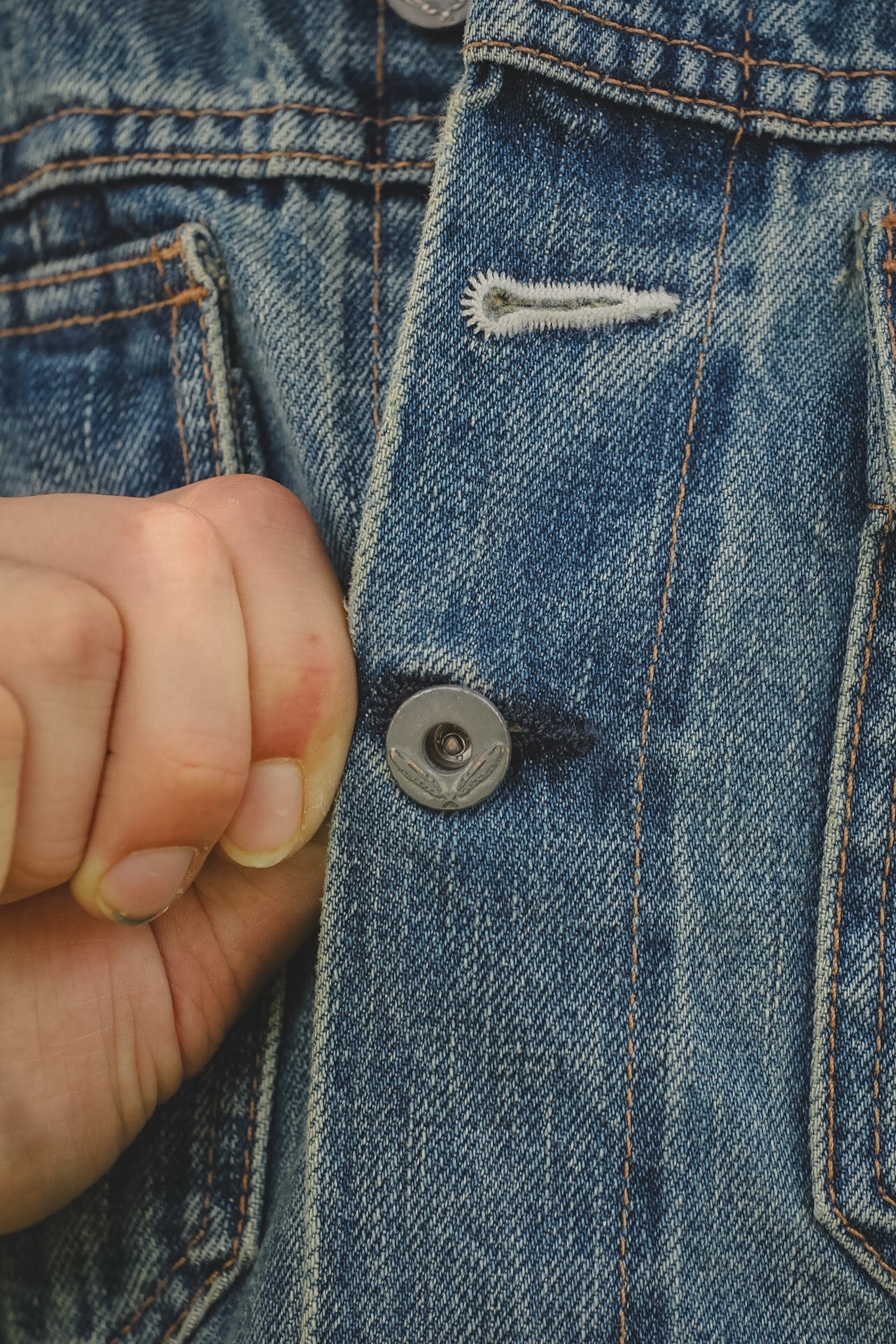 Close-up of a button on a blue denim jacket with a hand pressing it.