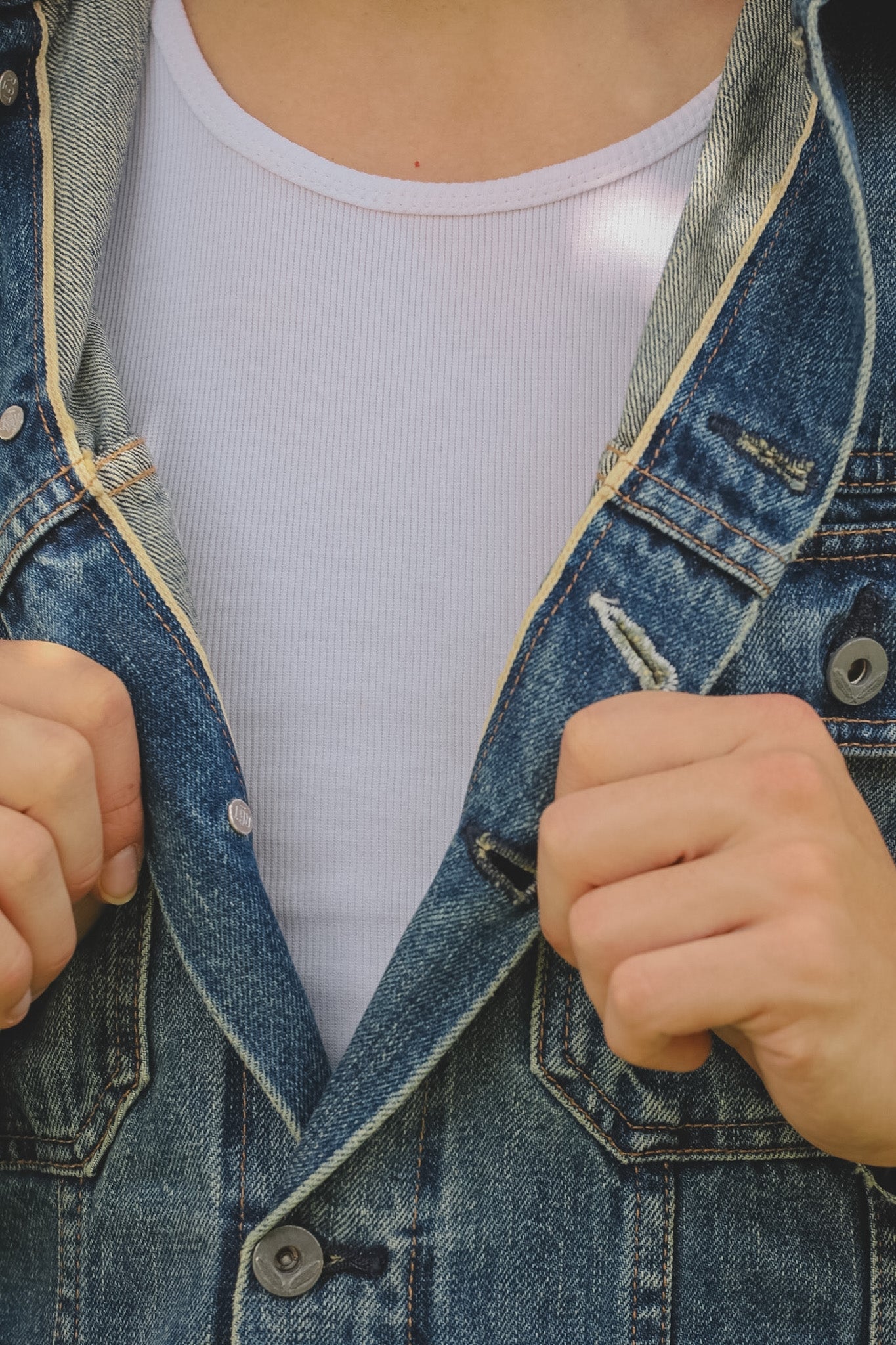 Person wearing a denim jacket over a white shirt with fists clenched.