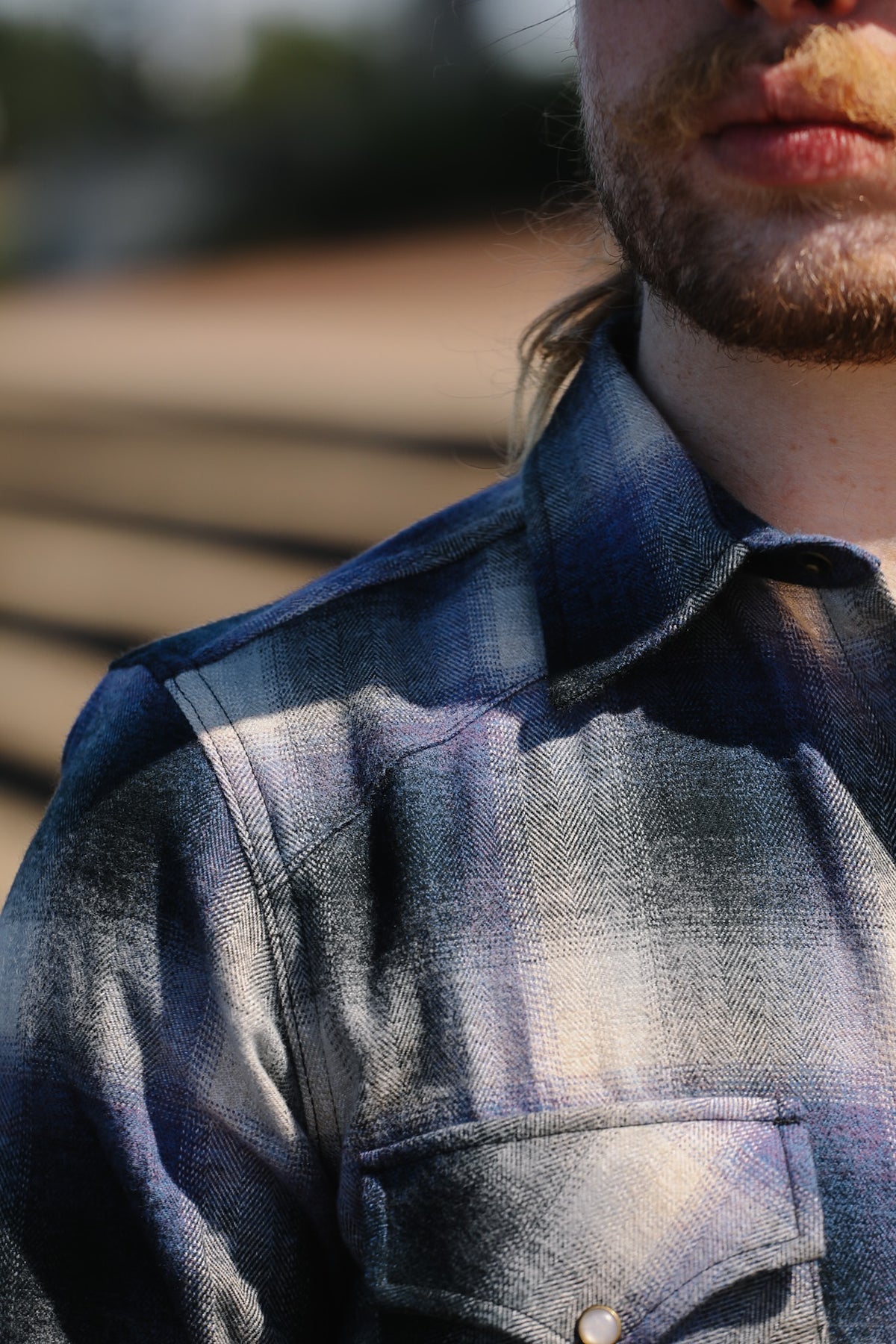 Close-up of a man wearing a blue and gray plaid flannel shirt outdoors, with sunlight casting shadows across the fabric.