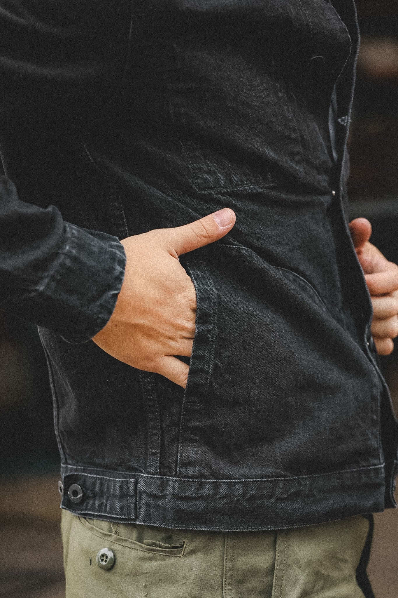 Person wearing a black jacket with one hand in the pocket, blurred background