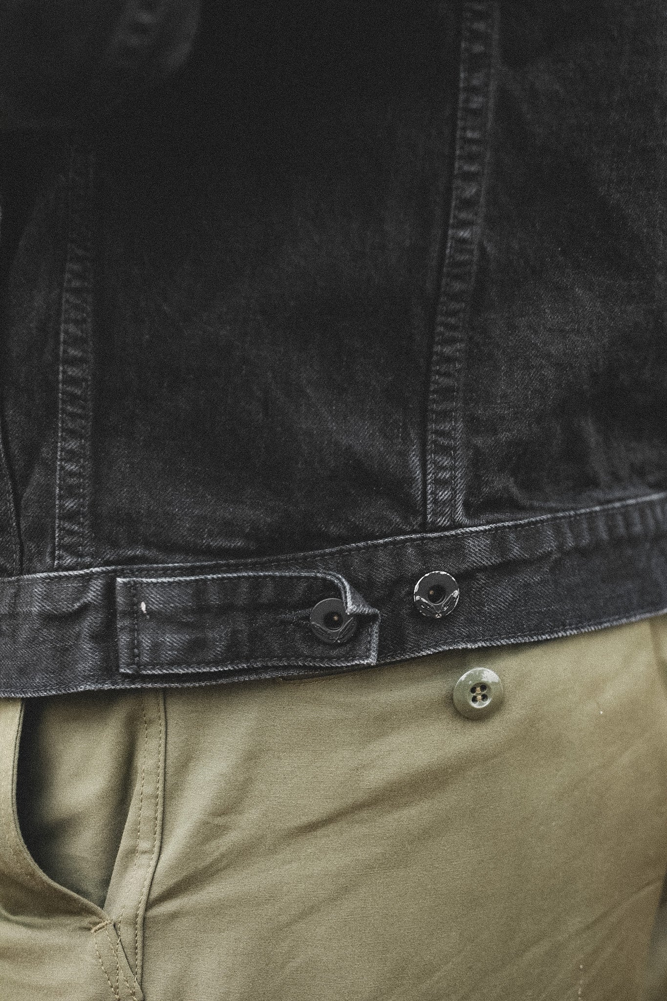 Close-up of a black jacket and beige pants with visible buttons.