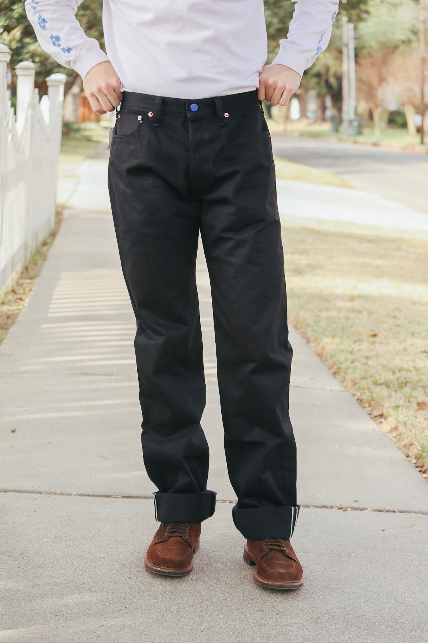Person wearing black pants and brown shoes on a sidewalk