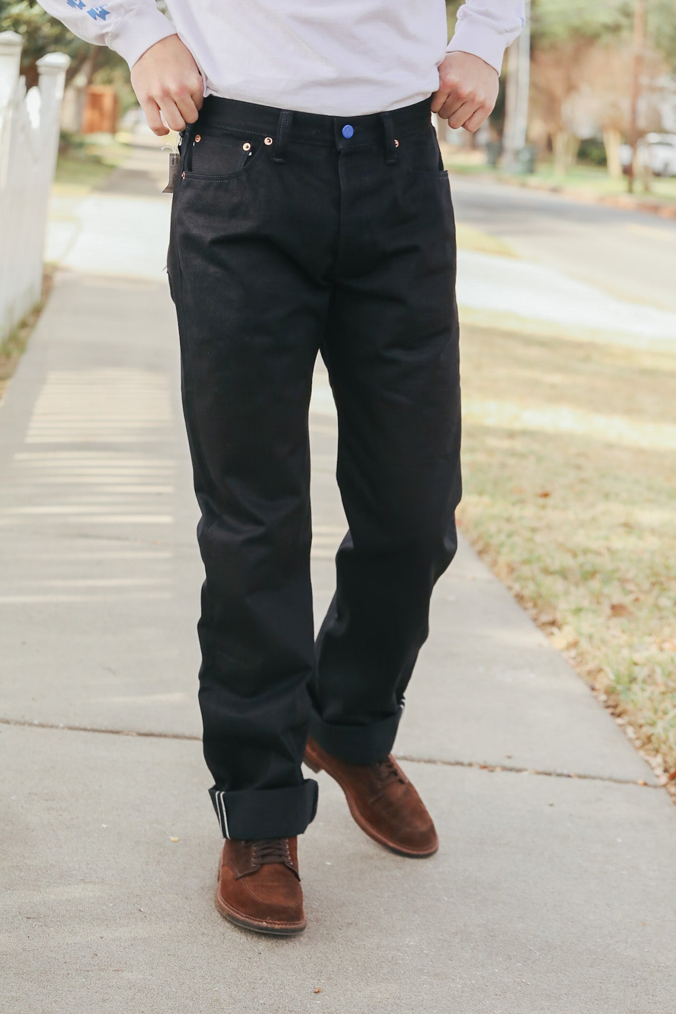 Person wearing black pants and brown shoes on a sidewalk