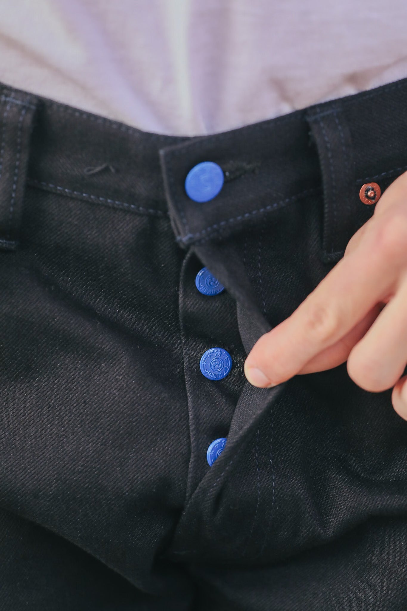 Close-up of a person buttoning a black shirt with blue buttons.