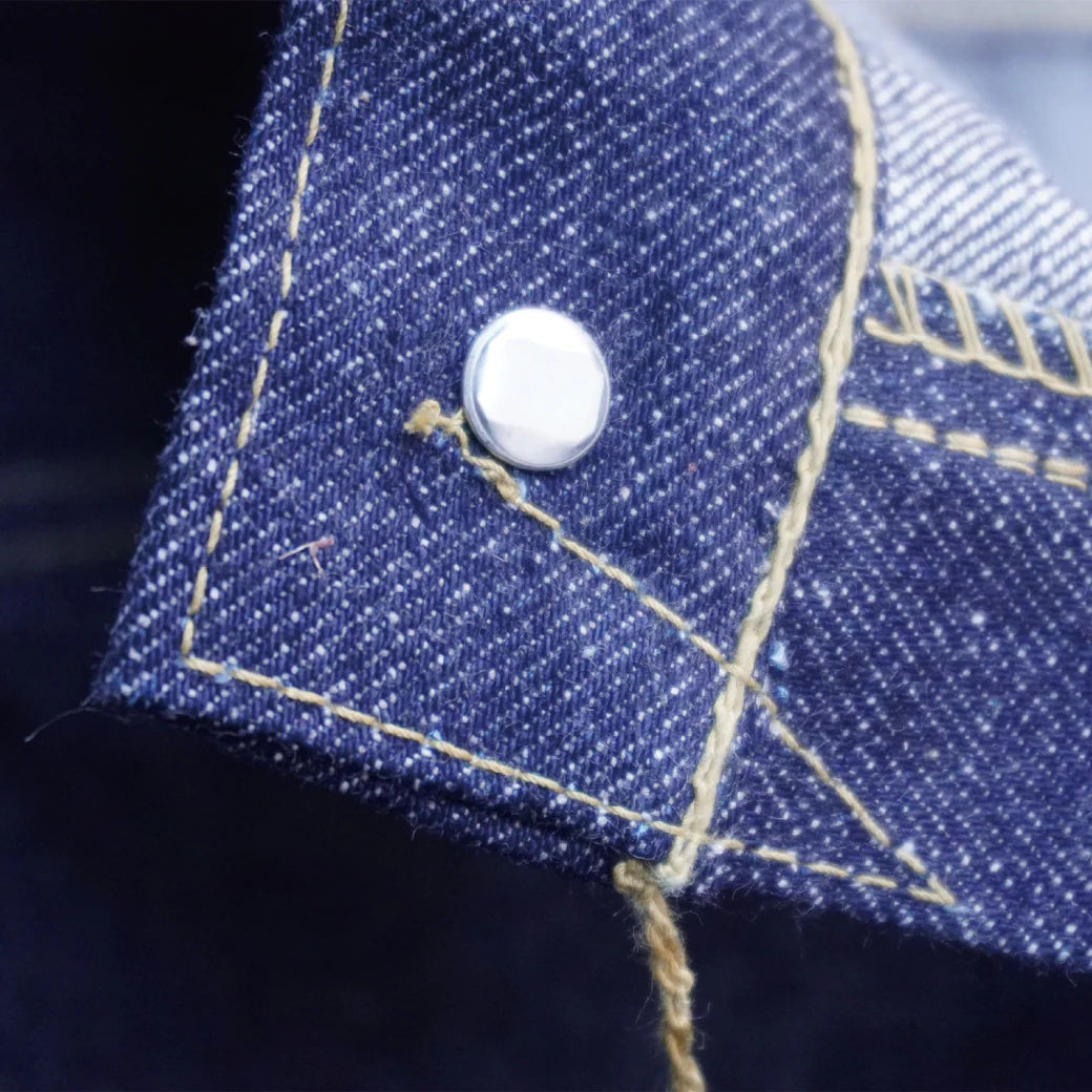 Close-up of blue denim fabric with white metal rivet and yellow stitching detail