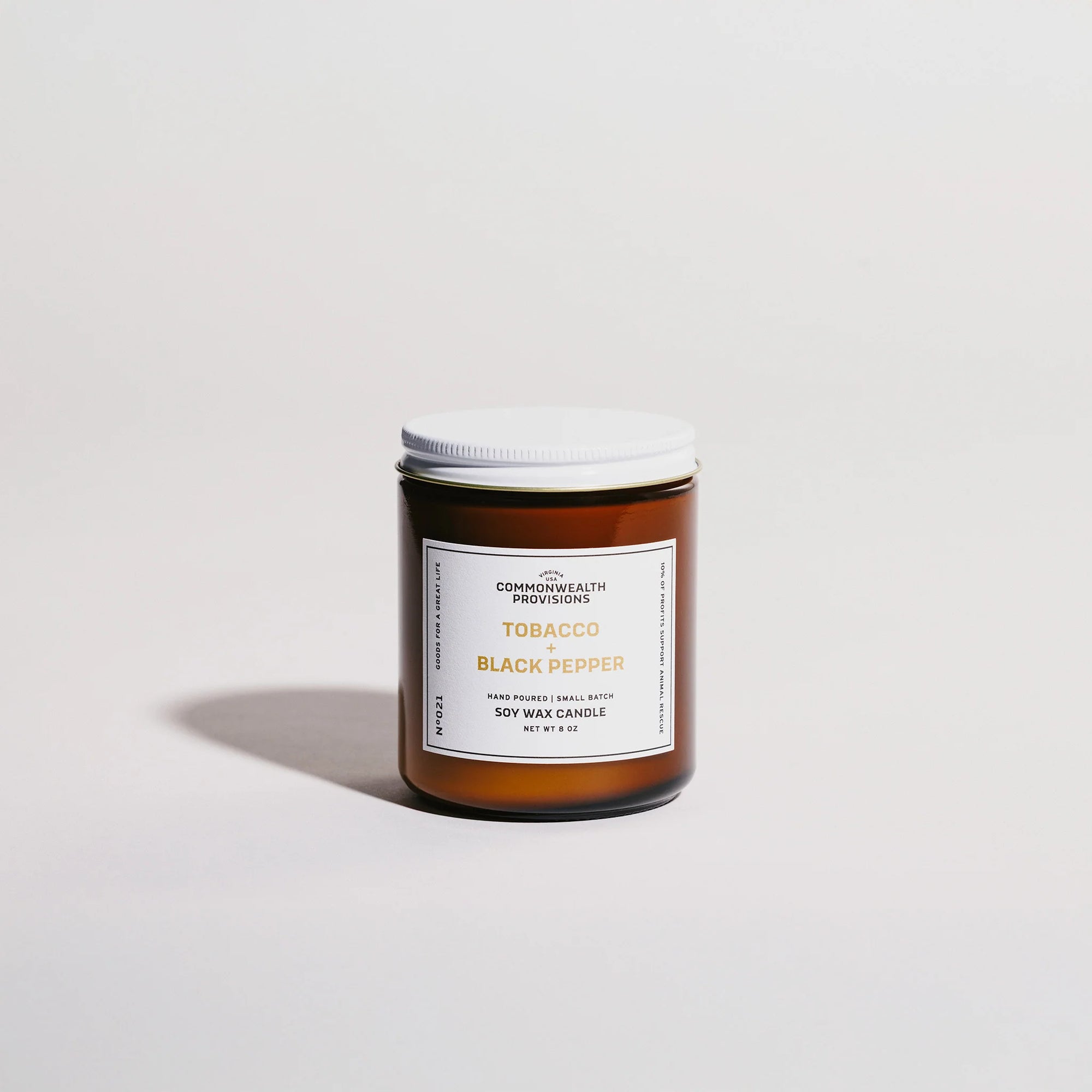 Amber glass jar of Commonwealth Provisions Tobacco and Black Pepper soy wax candle with white lid on light background