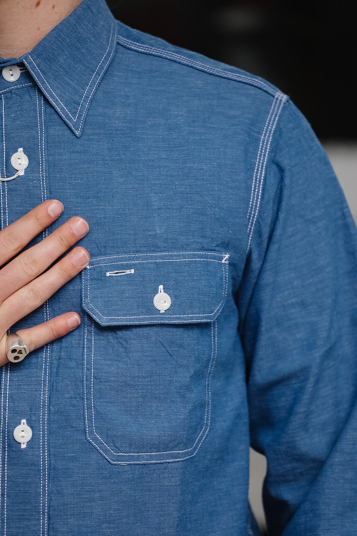 Close-up of a blue denim shirt with a hand touching the chest pocket.