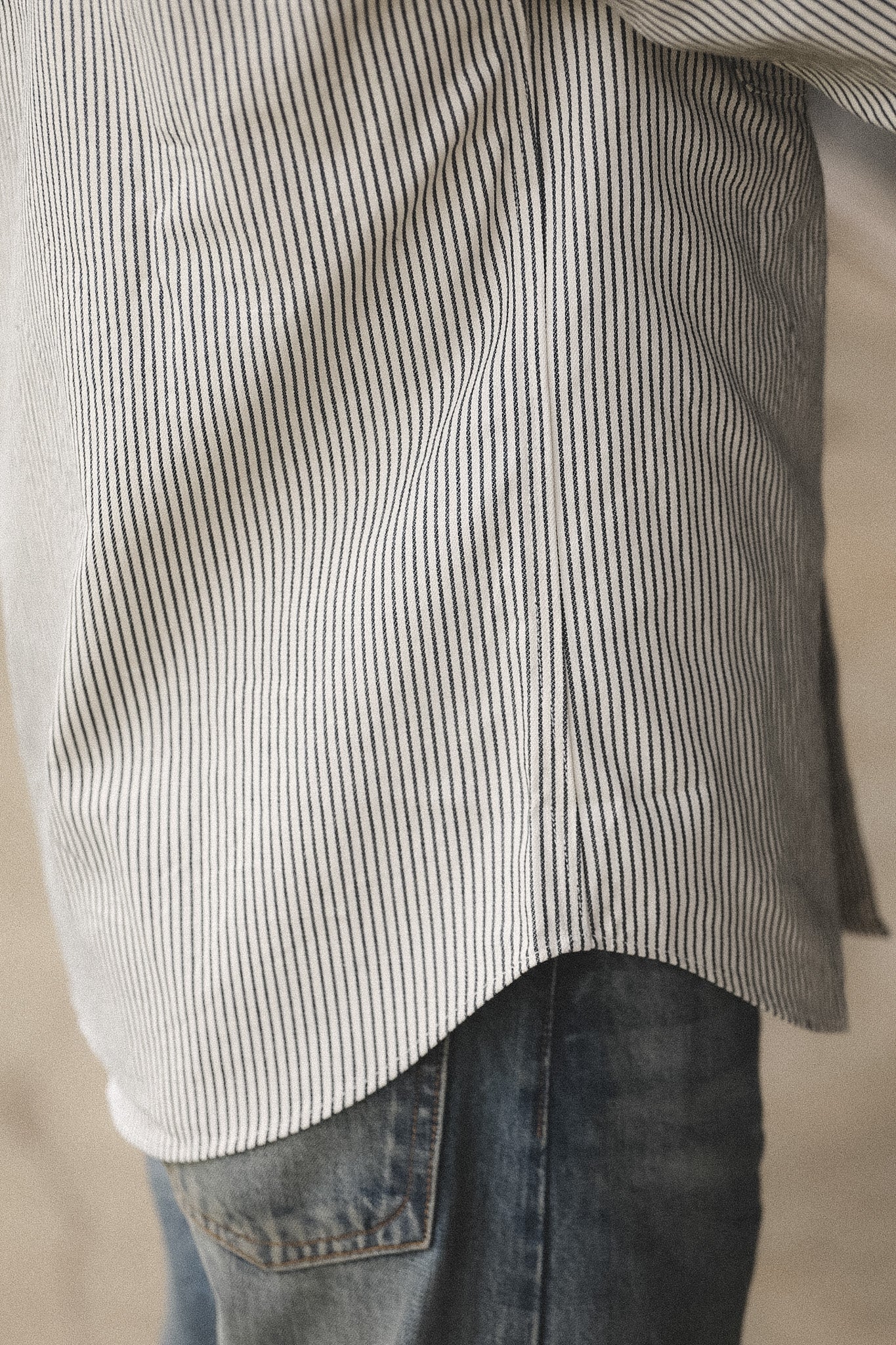 Close-up of a person wearing a striped shirt and jeans against a neutral background