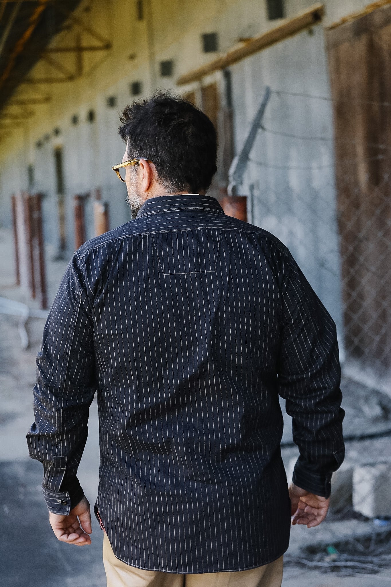 Man wearing a dark pinstripe shirt standing in an industrial setting.