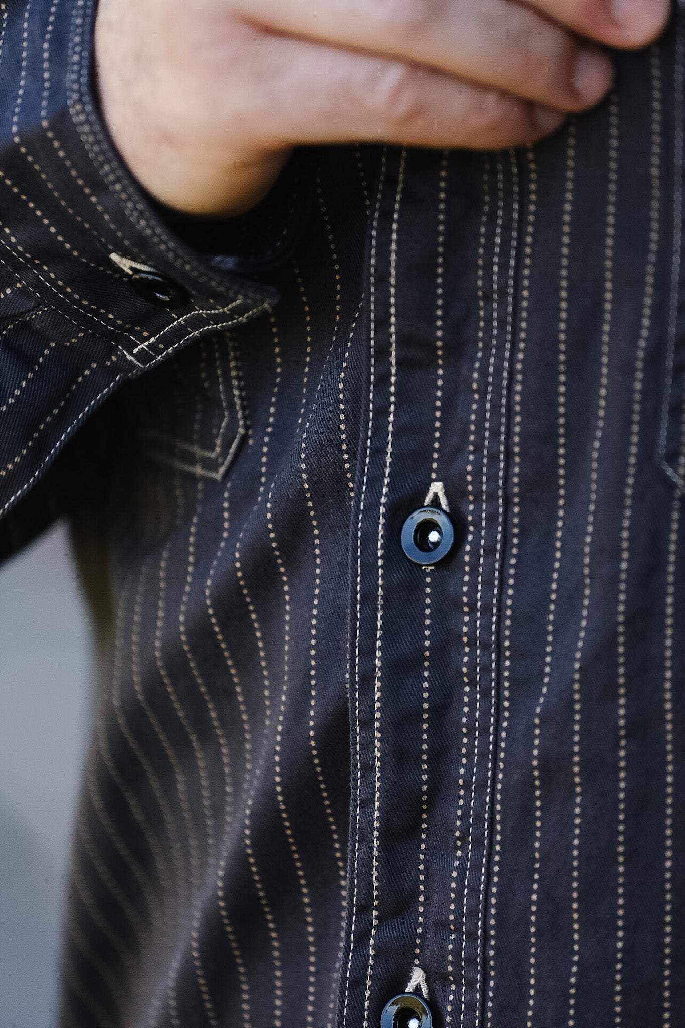Close-up of a dark blue pinstripe shirt with a button being adjusted.