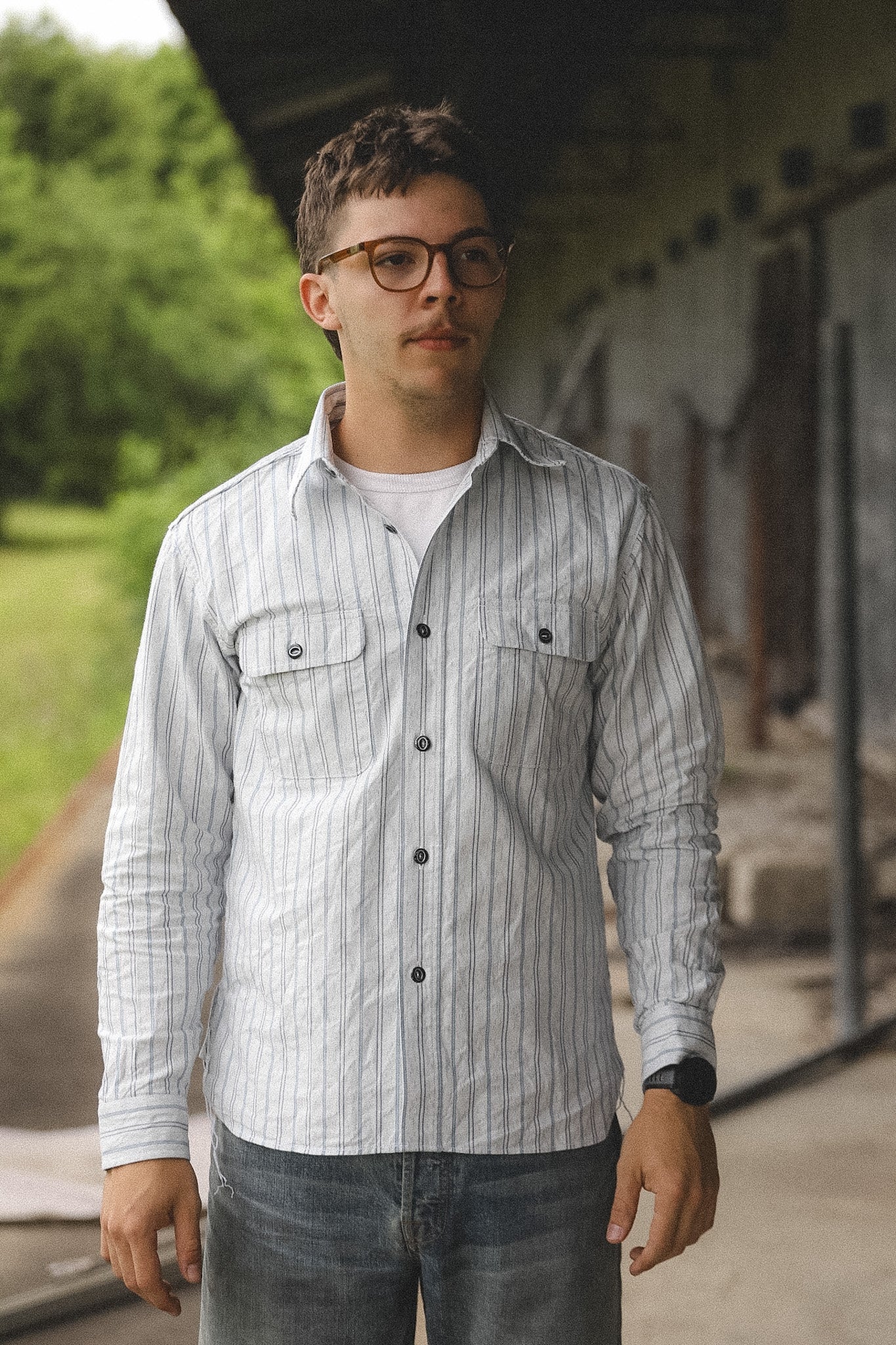 Man wearing a striped shirt and glasses standing outdoors.