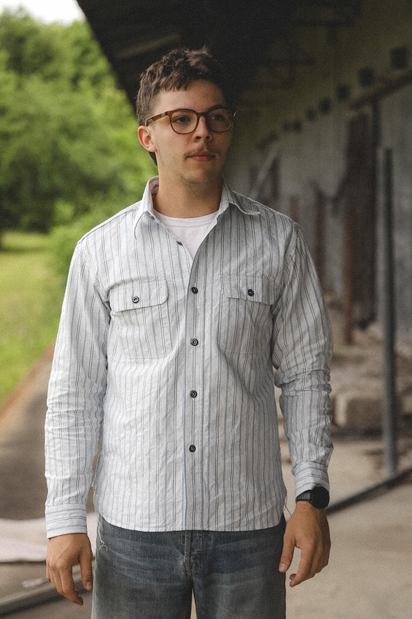Man wearing a striped shirt and glasses standing outdoors.