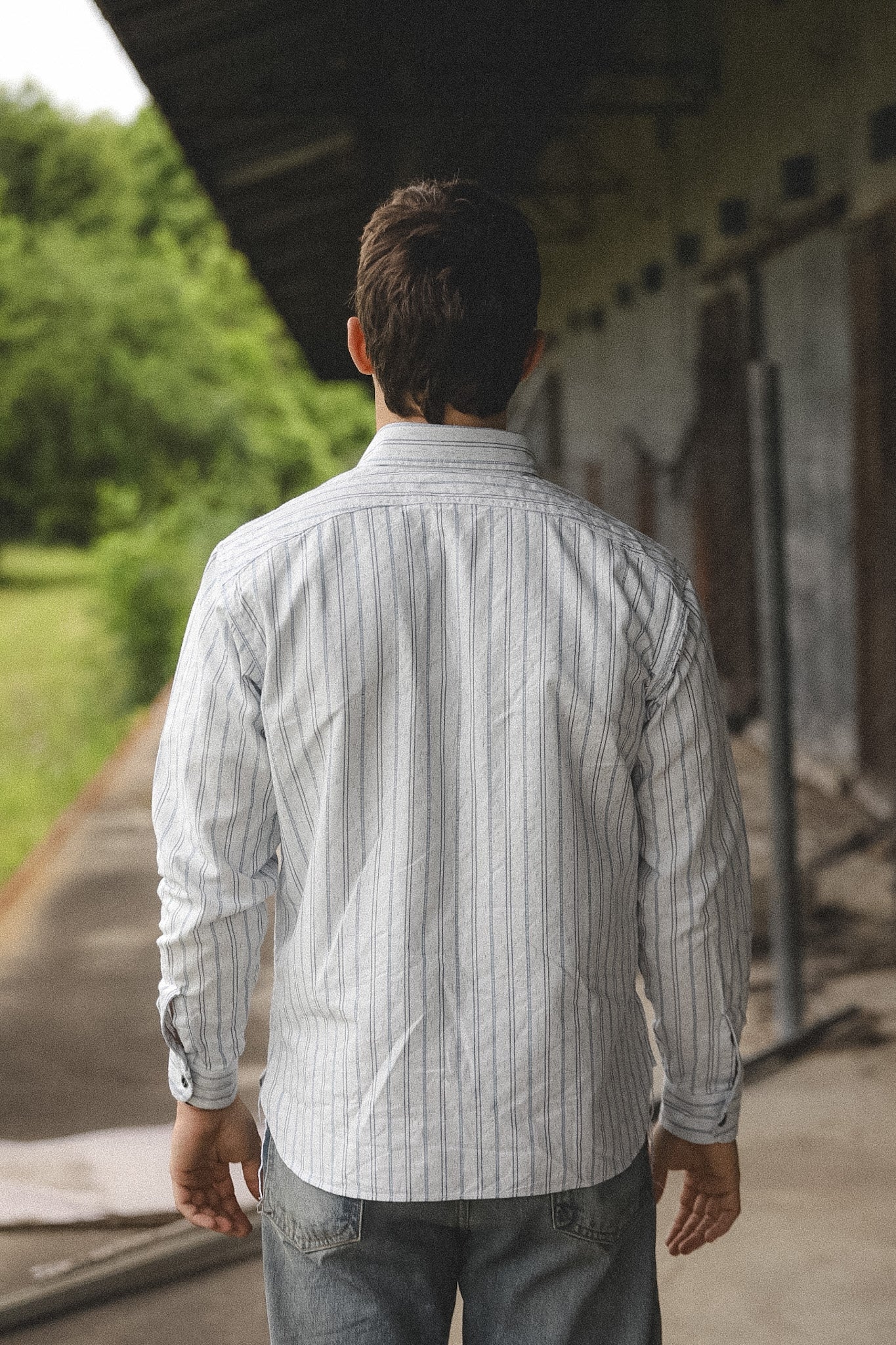 Man standing on a platform looking towards a building with greenery in the background