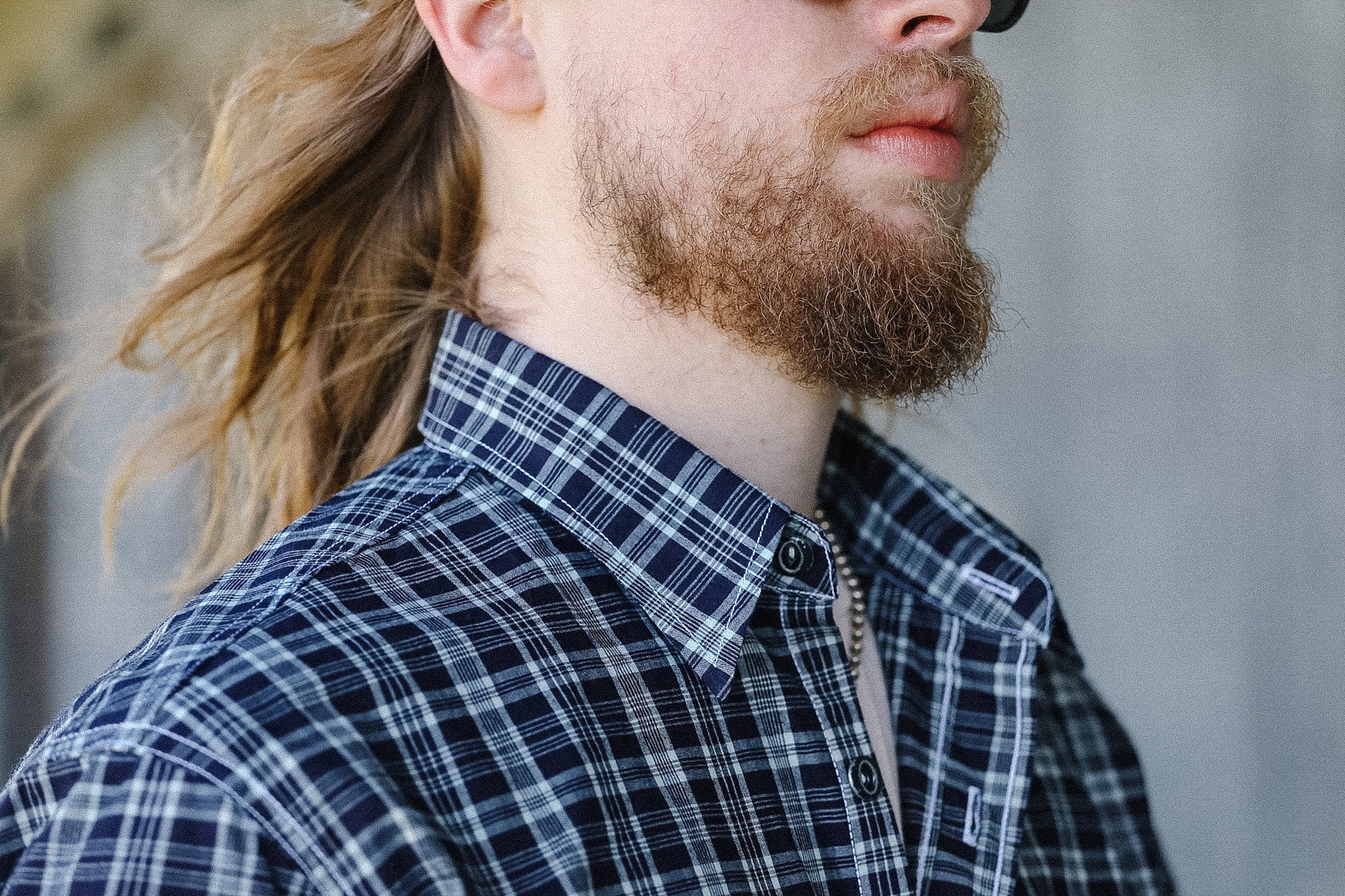 Man with a beard wearing a plaid shirt against a blurred background