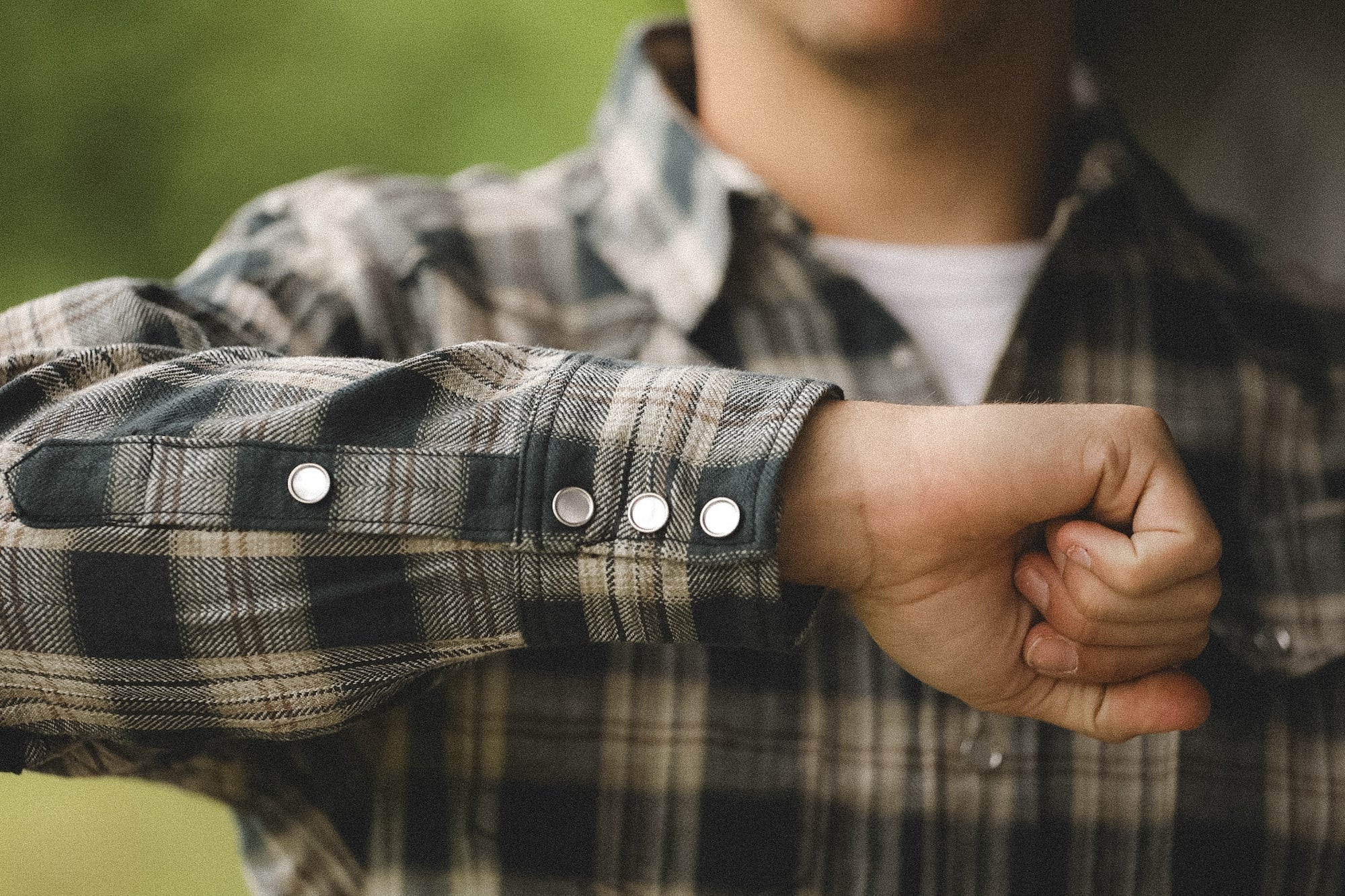 Person wearing a plaid shirt with rolled-up sleeves, outdoors.