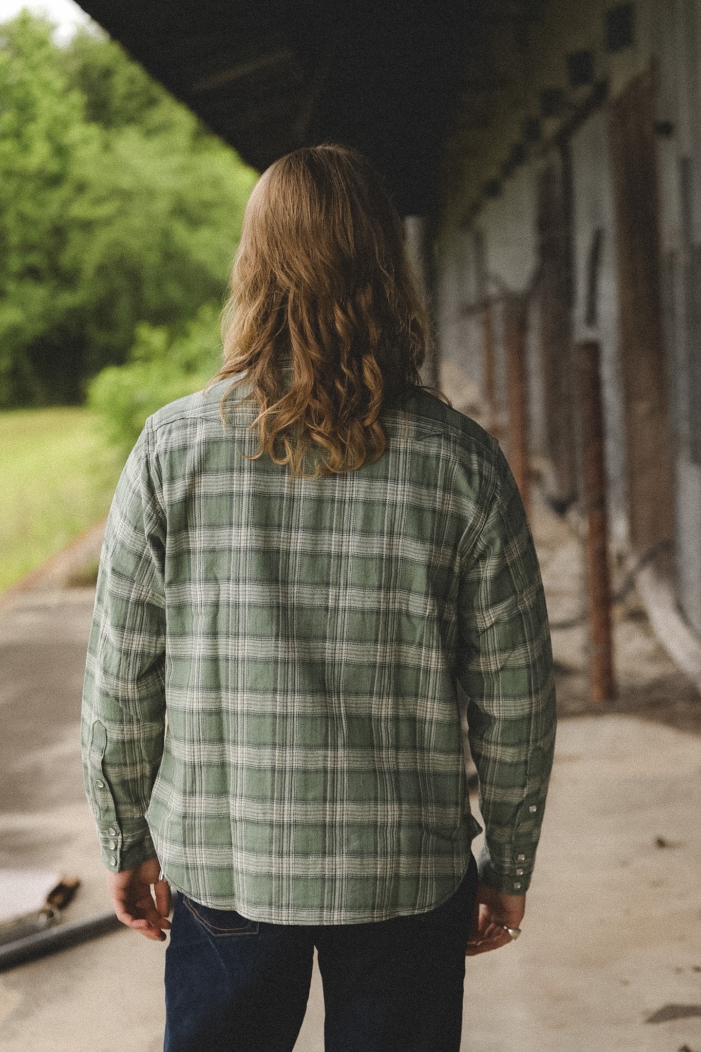 Person wearing a green plaid shirt walking away from the camera in an outdoor setting.