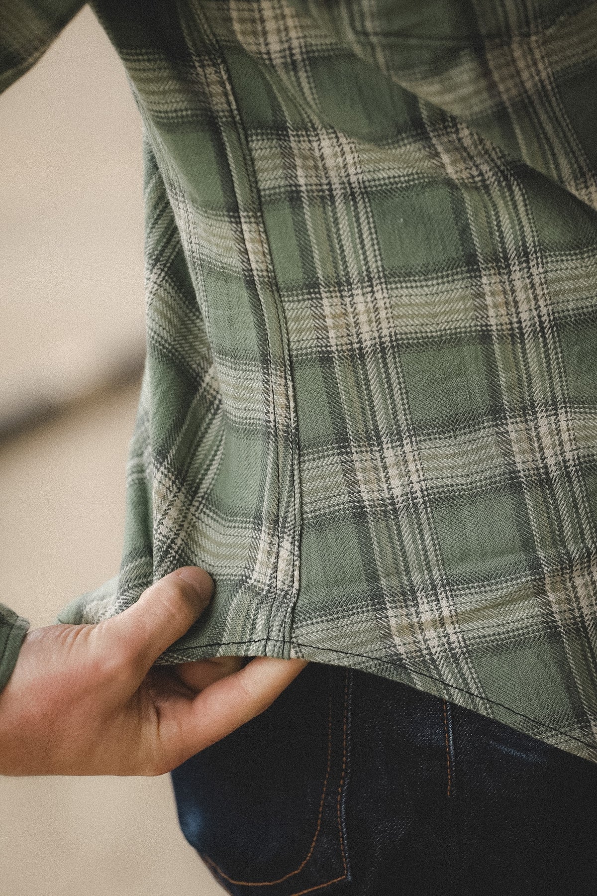 Close-up of a person holding a green plaid shirt with a blurred background