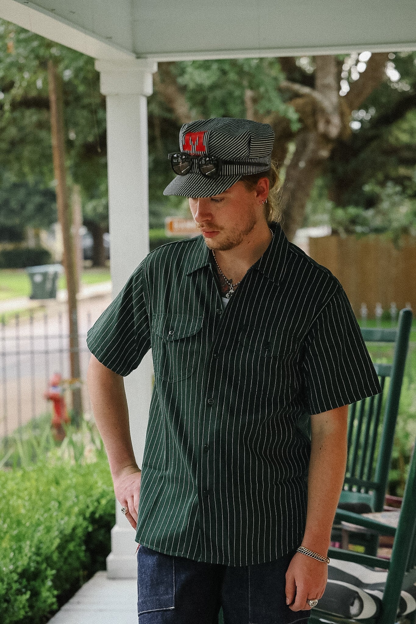 Man wearing a cap and striped shirt on a porch with greenery in the background