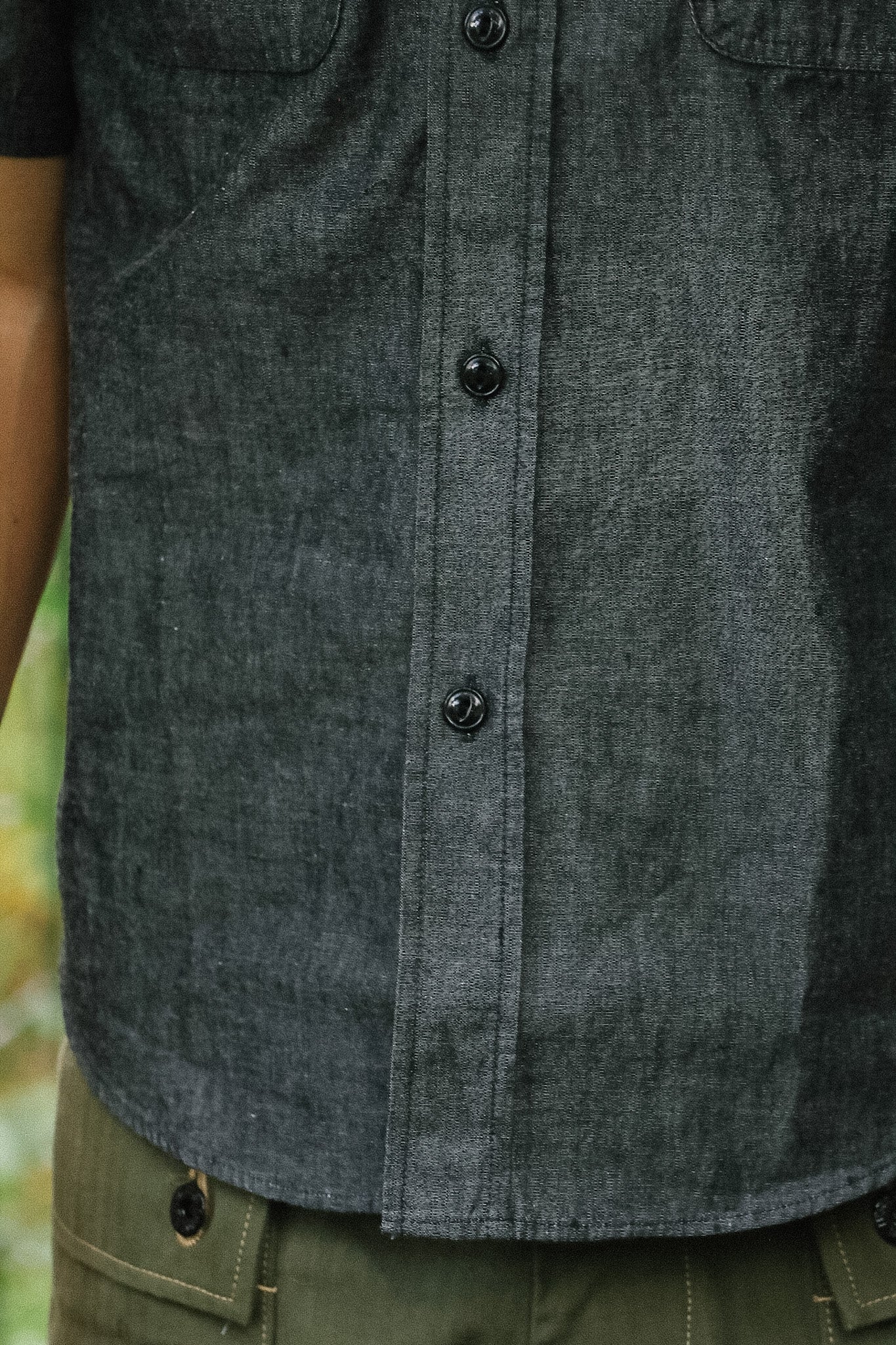 Close-up of a person wearing a dark gray button-up shirt with a blurred natural background