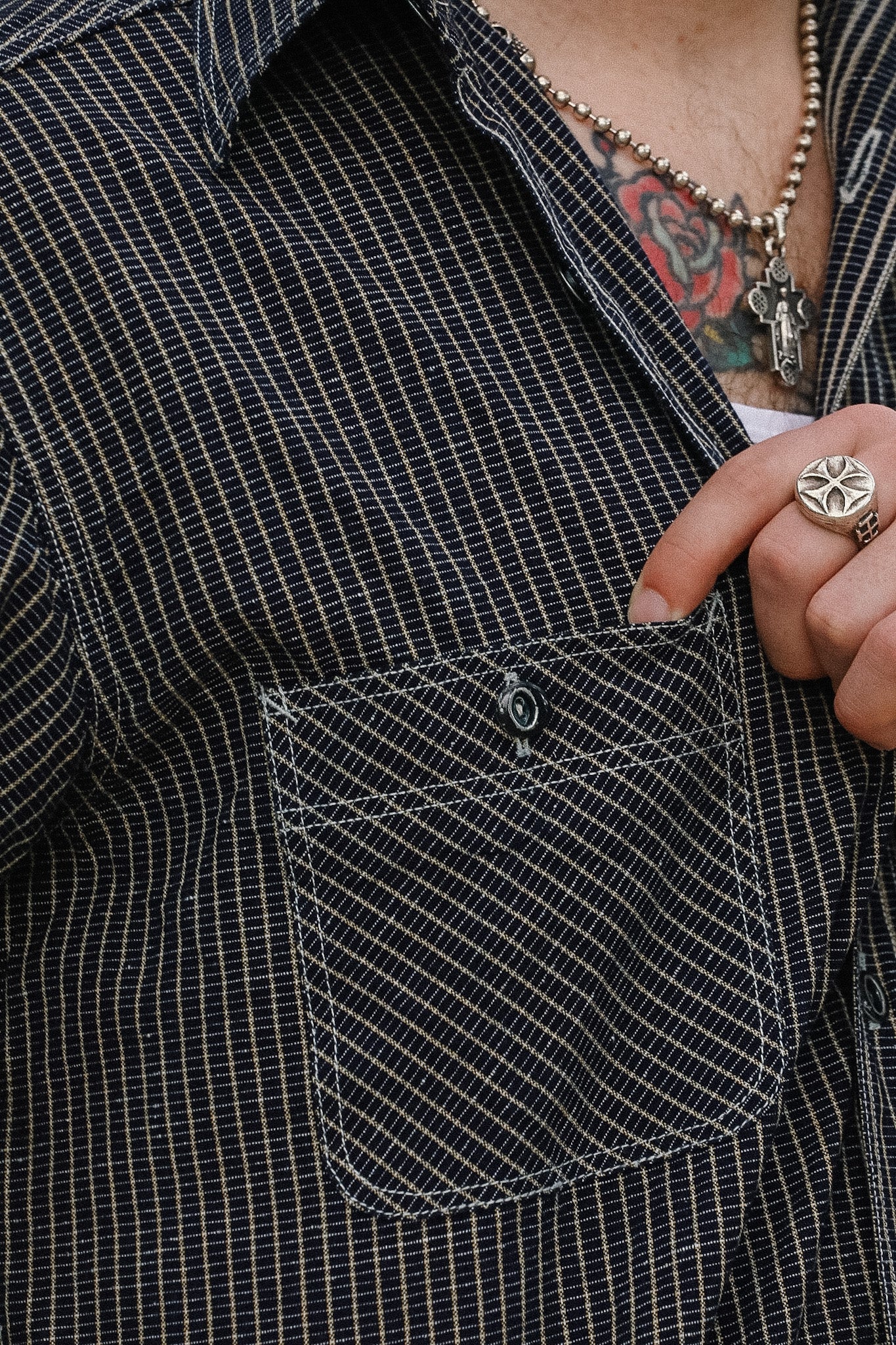 Person wearing a black checkered shirt with a pocket, showing a tattooed arm and ring.