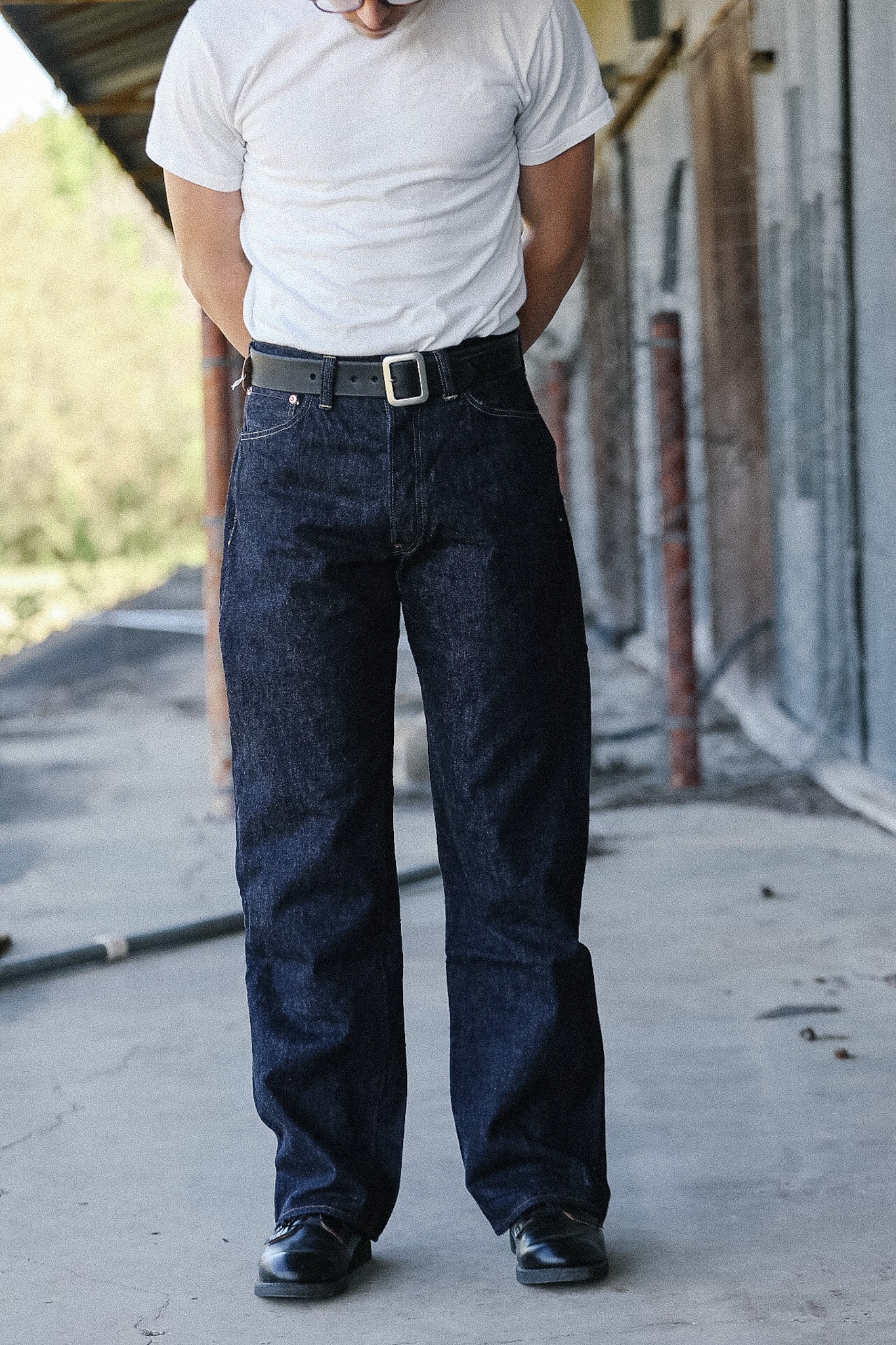 Person wearing a white t-shirt and dark blue jeans standing on a concrete surface.