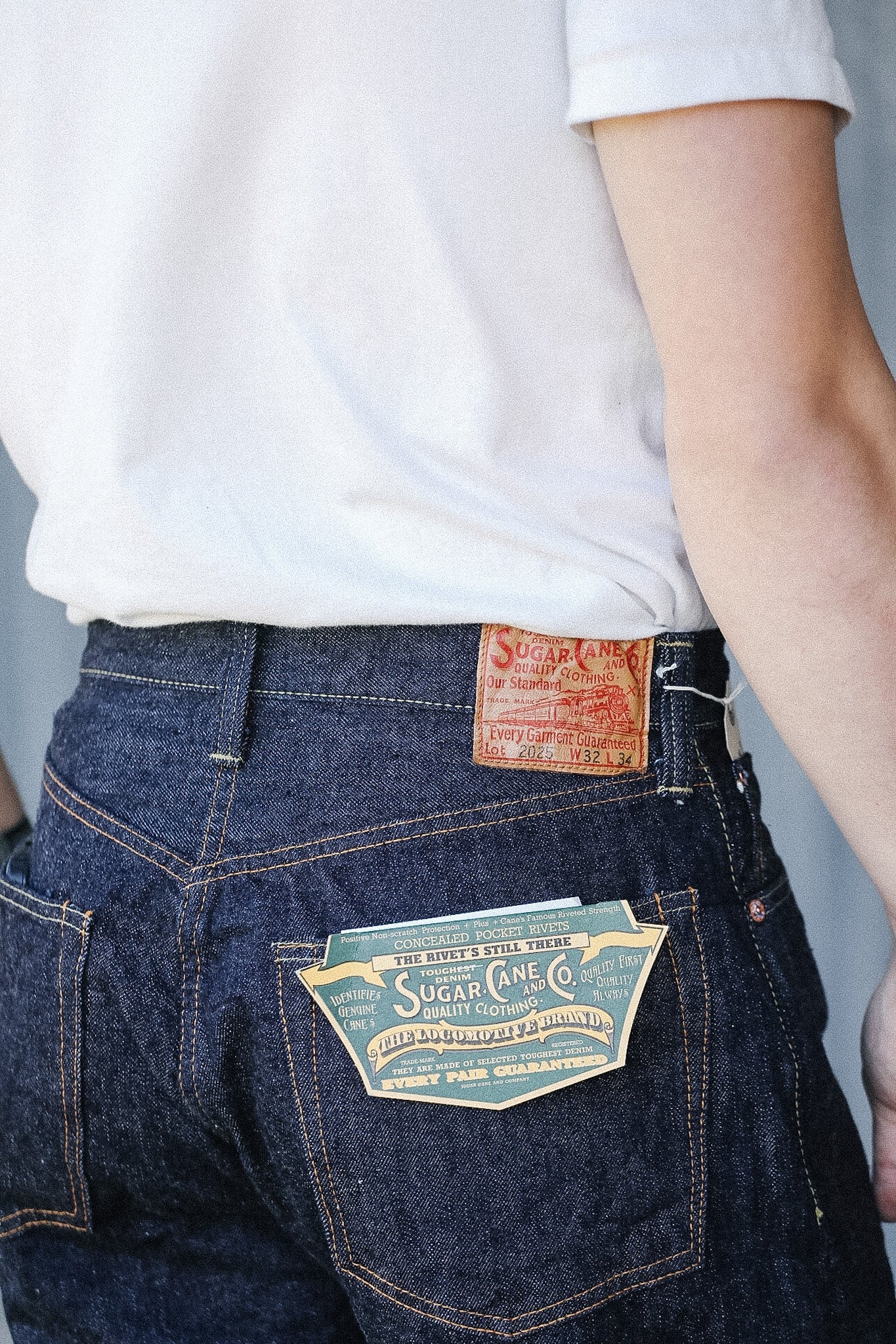 Person wearing blue jeans with a visible brand label against a plain background