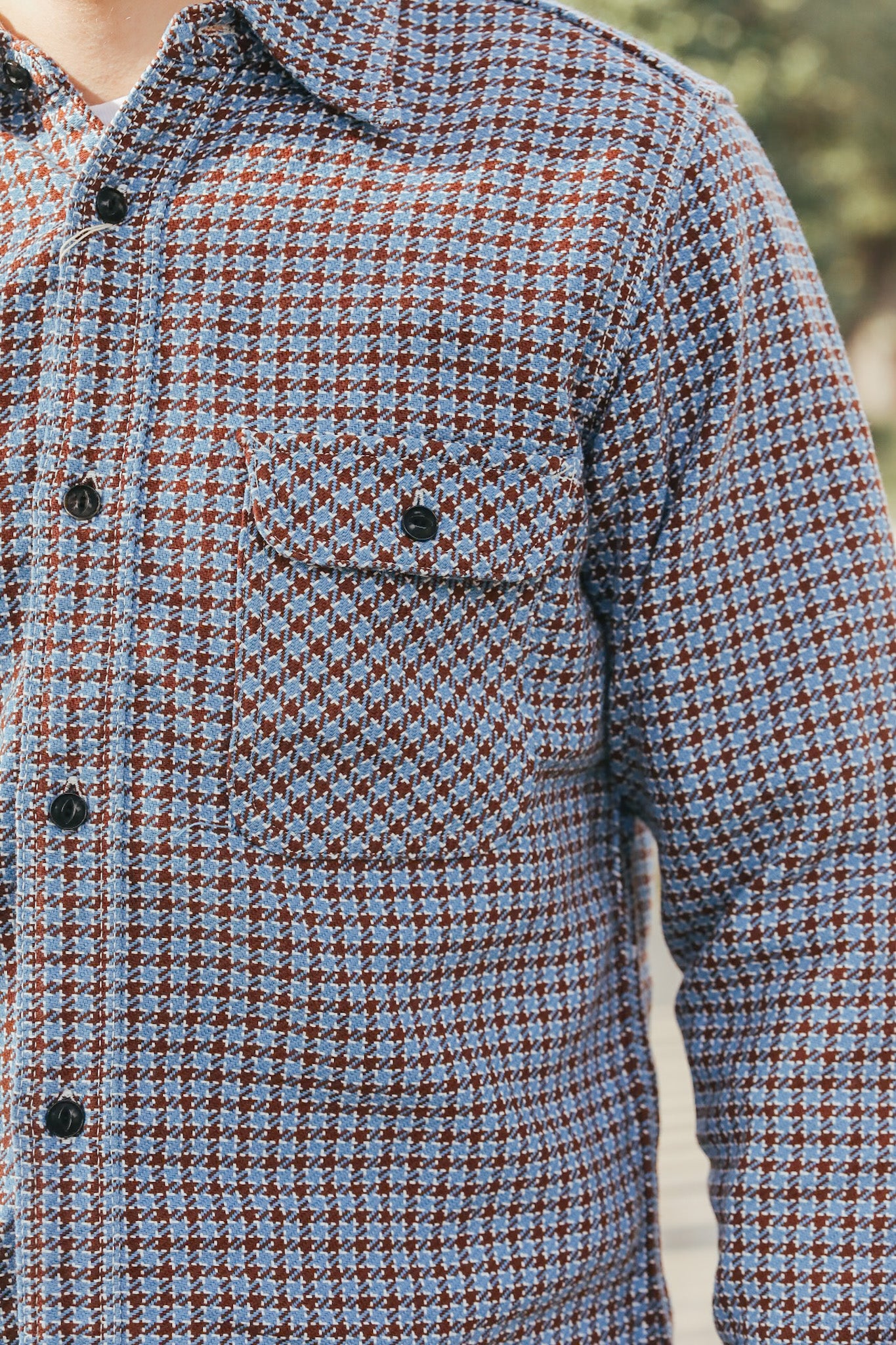 Houndstooth patterned shirt with black buttons on a blurred outdoor background