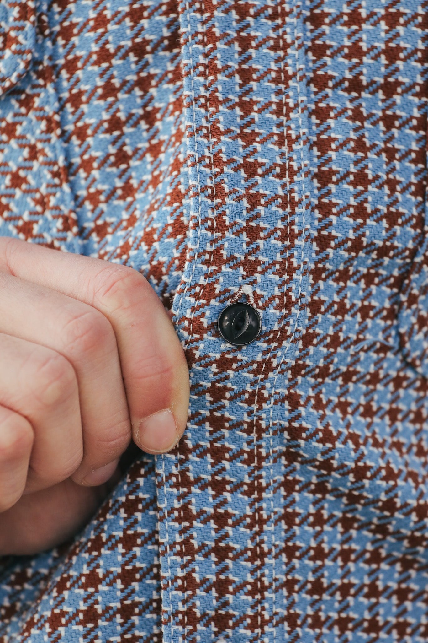 Close-up of a hand buttoning a blue and brown checkered shirt.