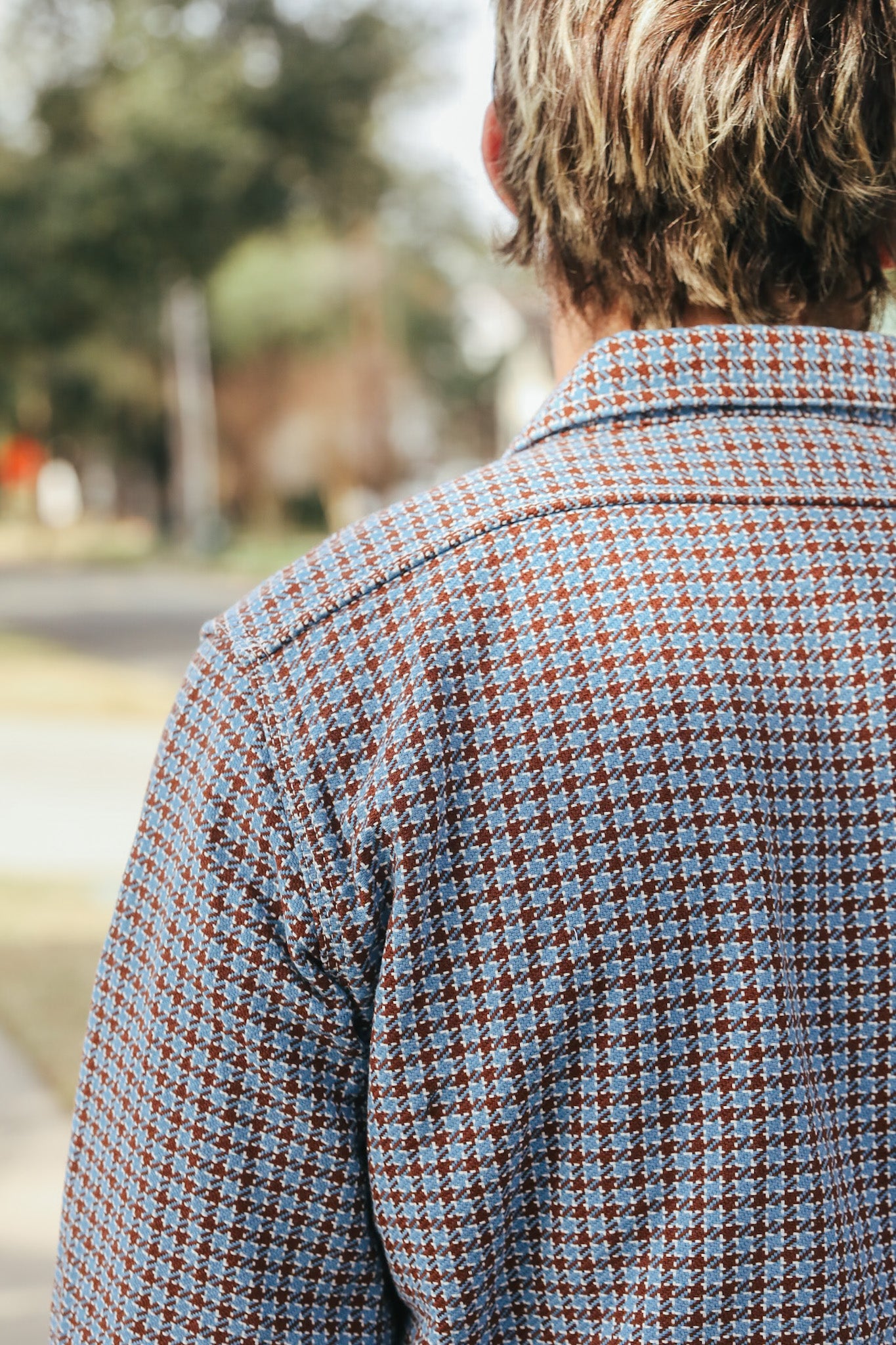 Person wearing a patterned shirt with a blurred outdoor background