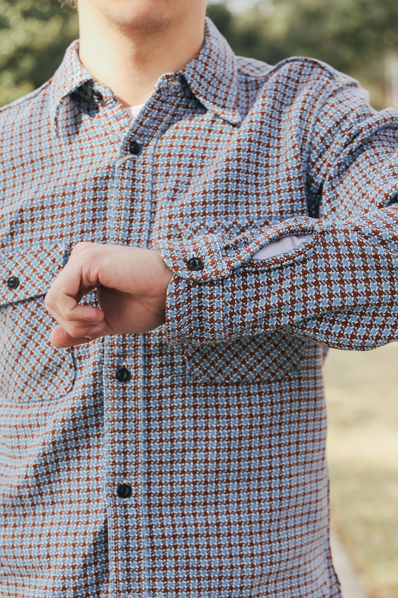 Close-up of a person wearing a plaid shirt with a blurred natural background