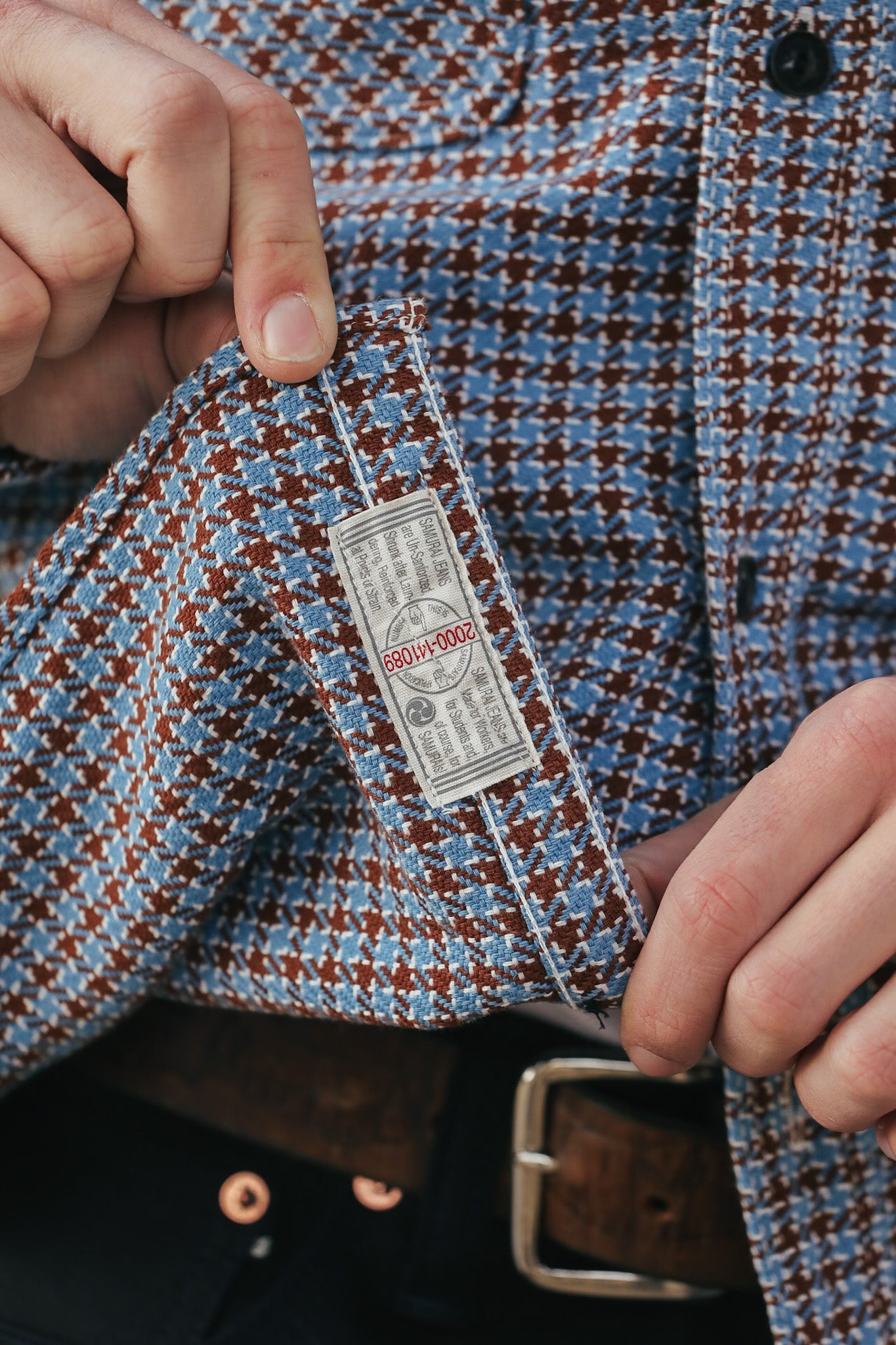 Close-up of a patterned shirt with a tag, held by hands.