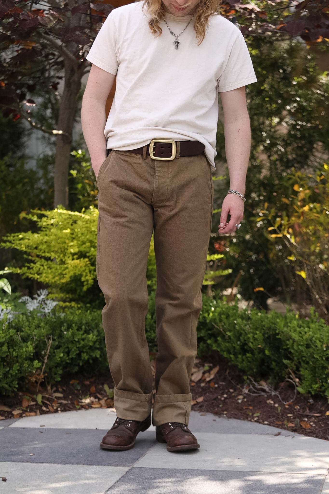 Person wearing a white t-shirt, brown pants, and brown shoes standing outdoors.
