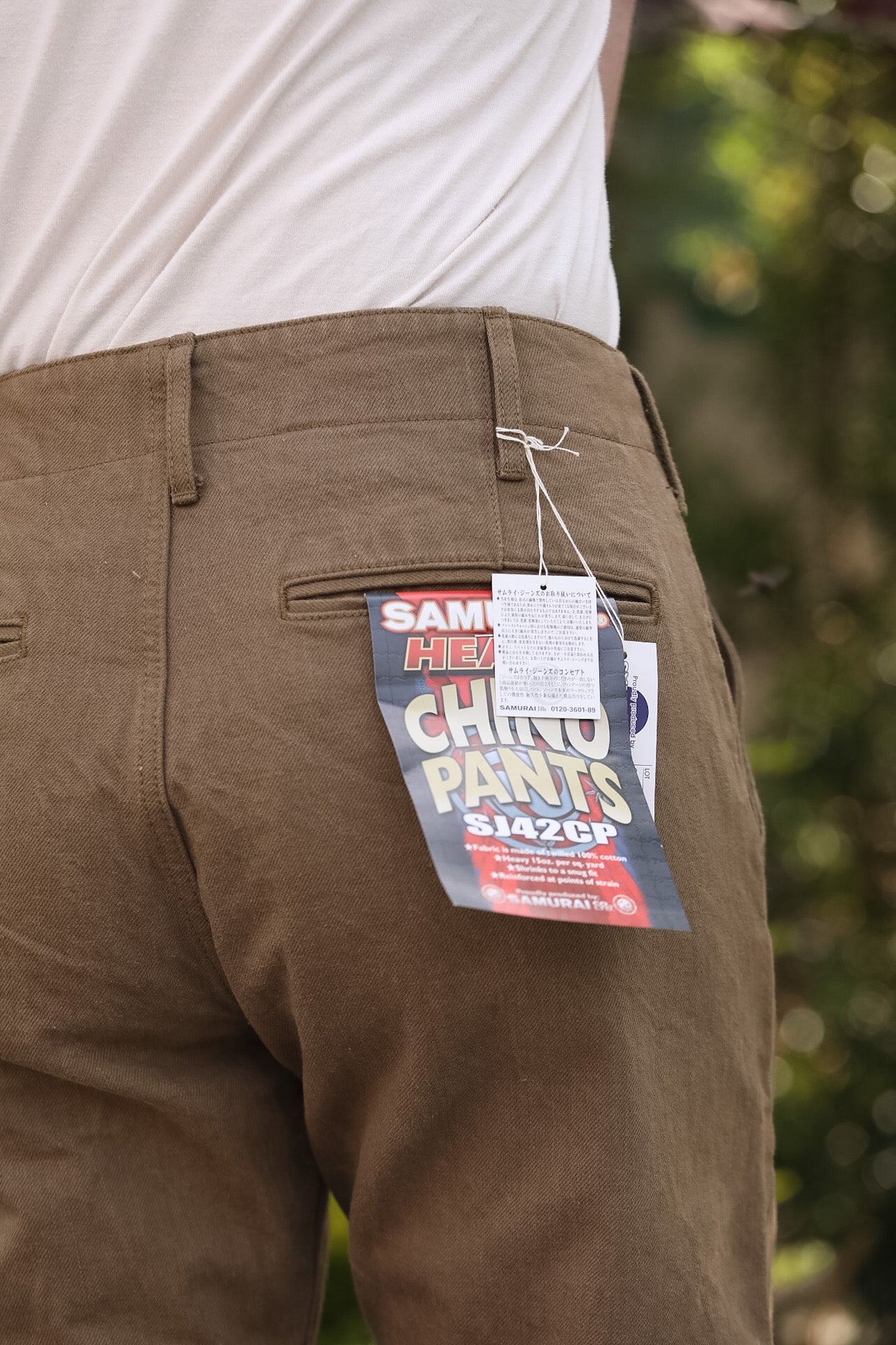 Brown chino pants with a tag on the back pocket, blurred green background