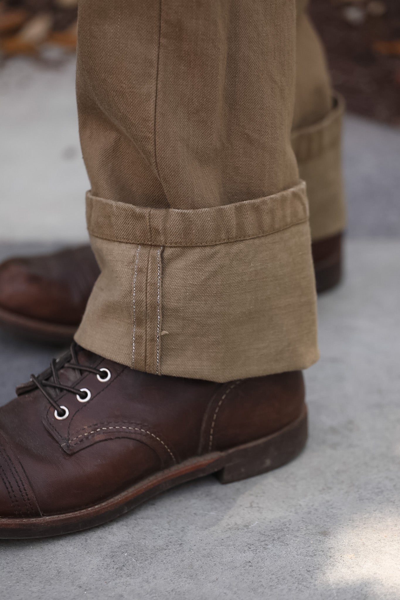 Close-up of brown leather shoes and beige pants on a concrete surface