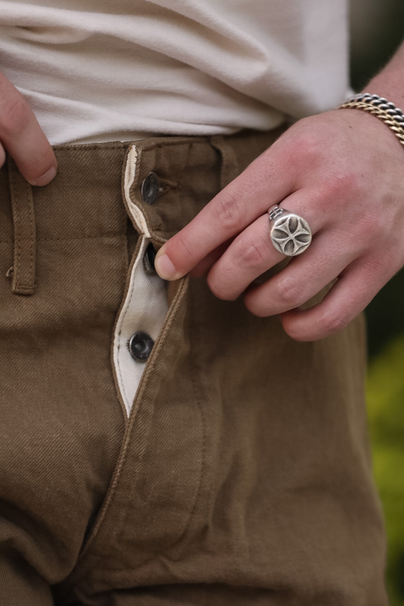 Close-up of a person wearing a silver ring on brown pants with a blurred green background
