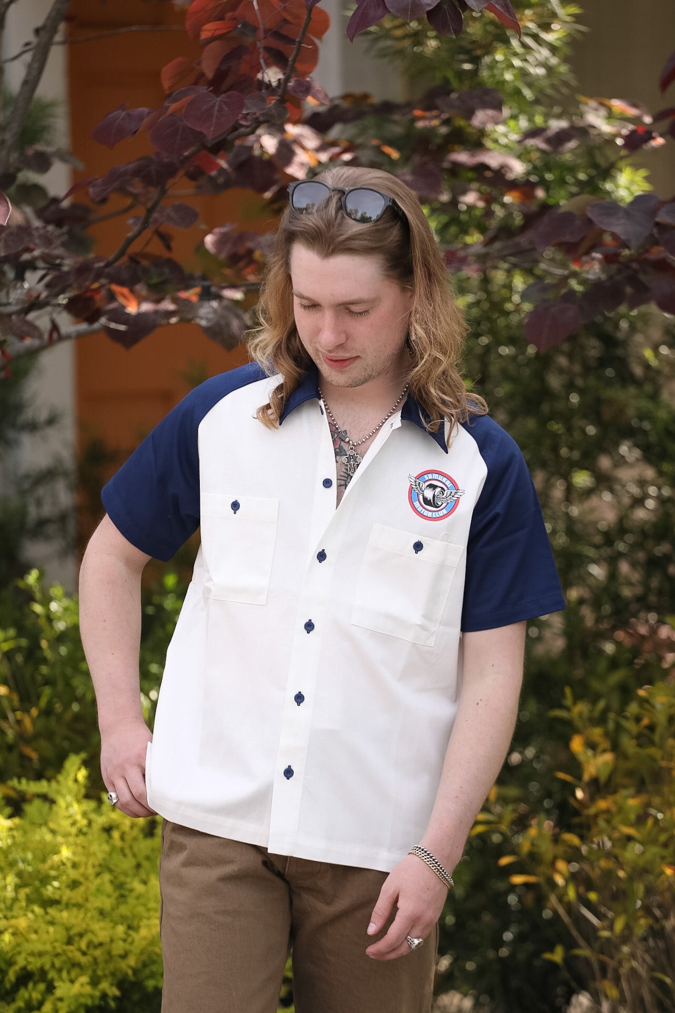 Man wearing a white shirt with a logo and navy sleeves outdoors
