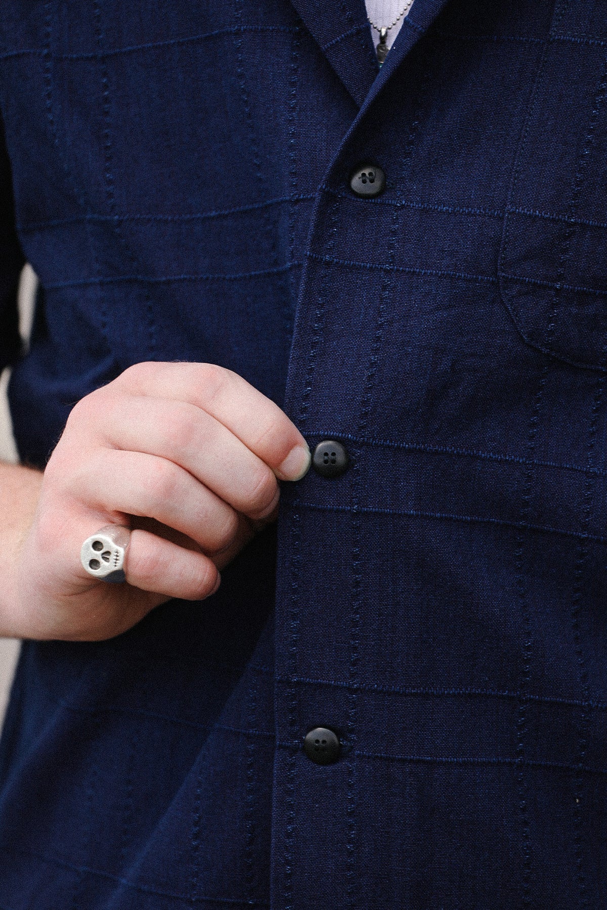 Close-up of a person wearing a dark navy textured button-up shirt, with a hand adjusting one of the buttons.