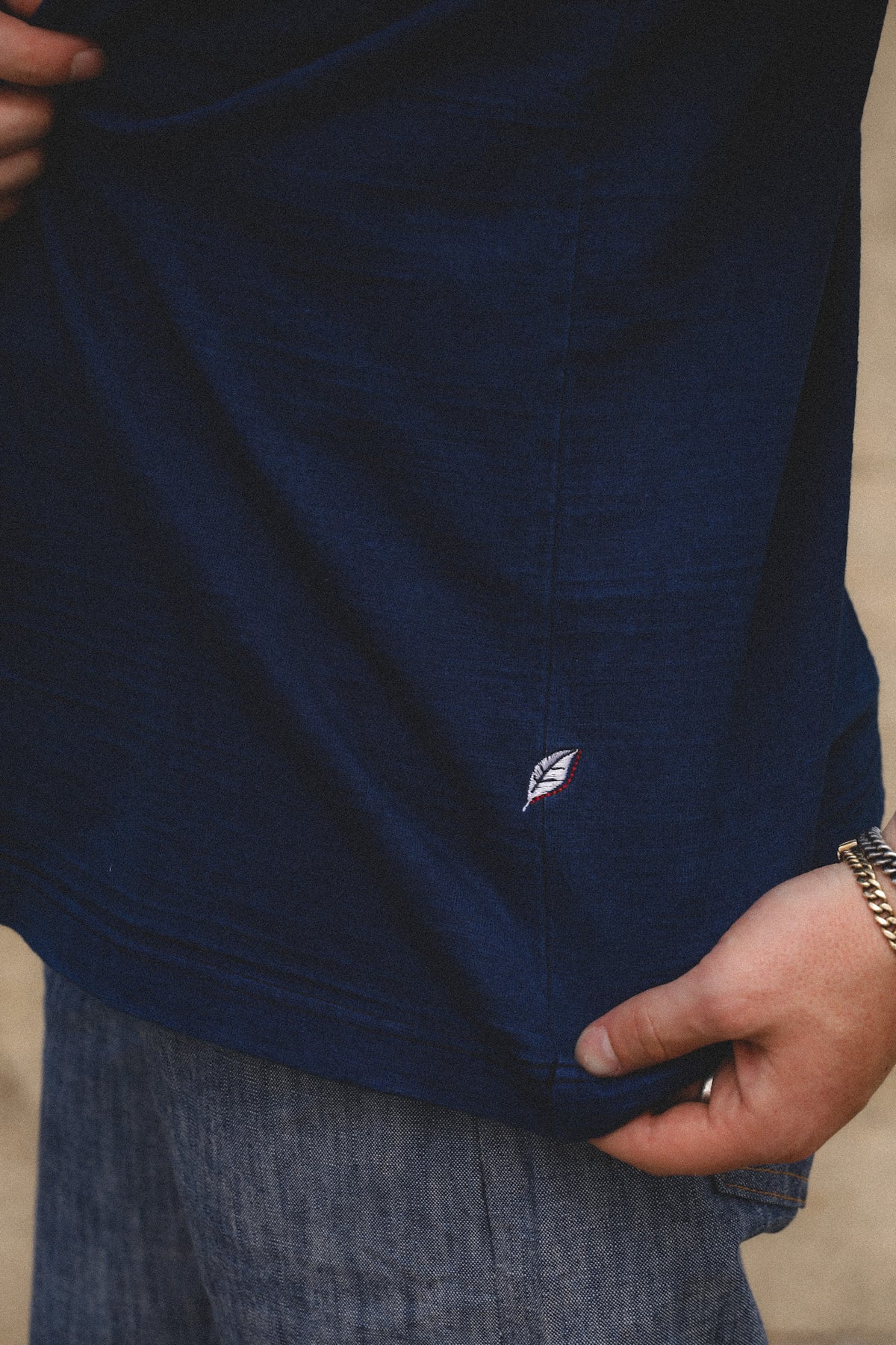 Close-up of a person wearing a dark navy blue t-shirt with a small embroidered logo on the lower front, paired with blue jeans.