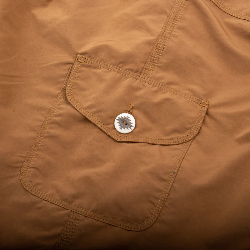 Close-up of brown workwear jacket pocket with decorative button detail, rugged stitching